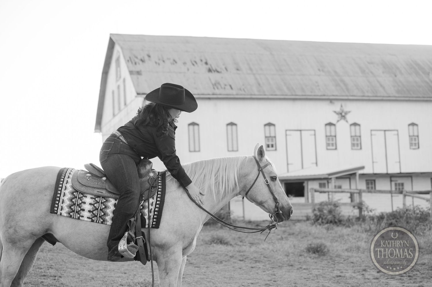 Vintage black and white photo of a rider on horseback near a large white barn building.