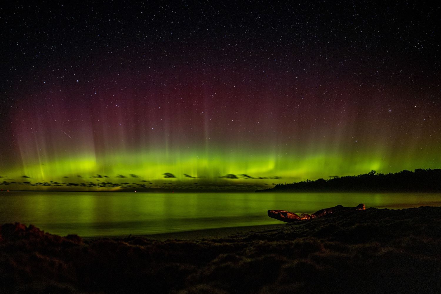Aurora borealis on the horizon with a reflection in water.
