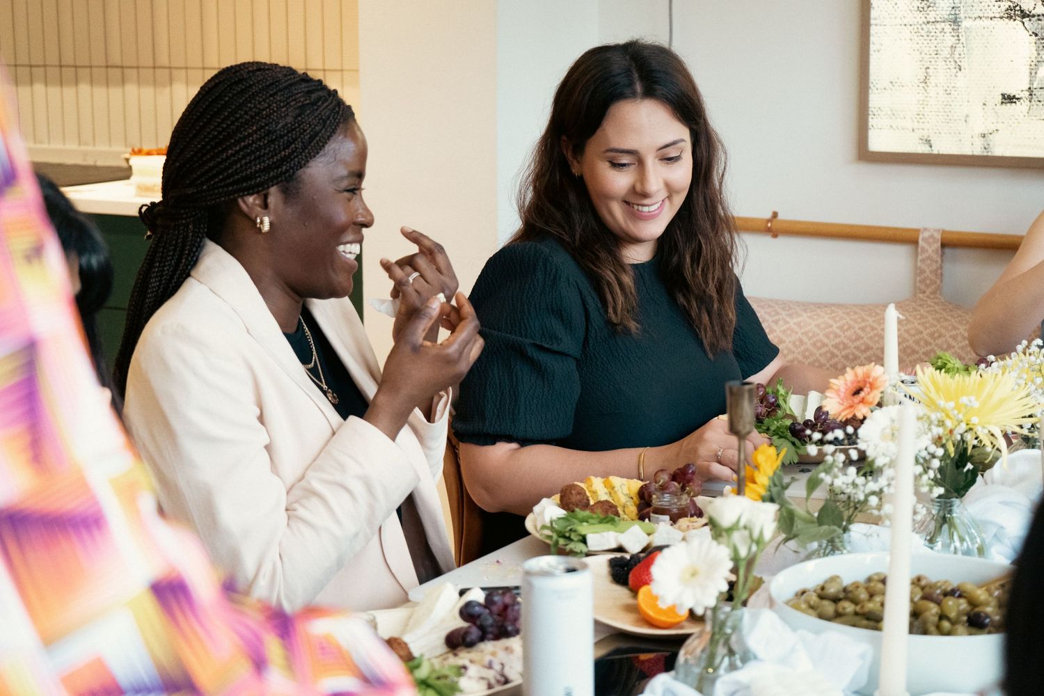 Two women smiling and enjoying food together at a beautifully decorated dining table with flowers and candles.