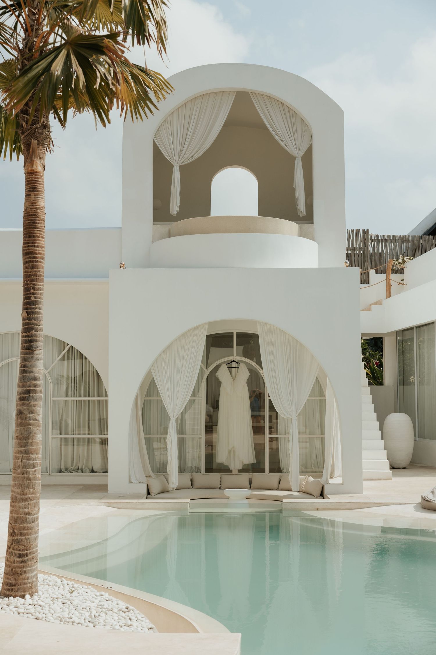 Elegant white Mediterranean-style building with arched doorways and a swimming pool surrounded by palm trees.