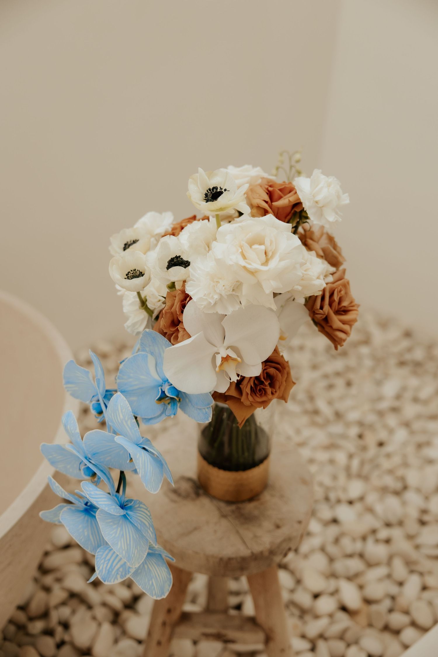 A romantic floral arrangement with white and brown flowers and light blue orchids in a vase.