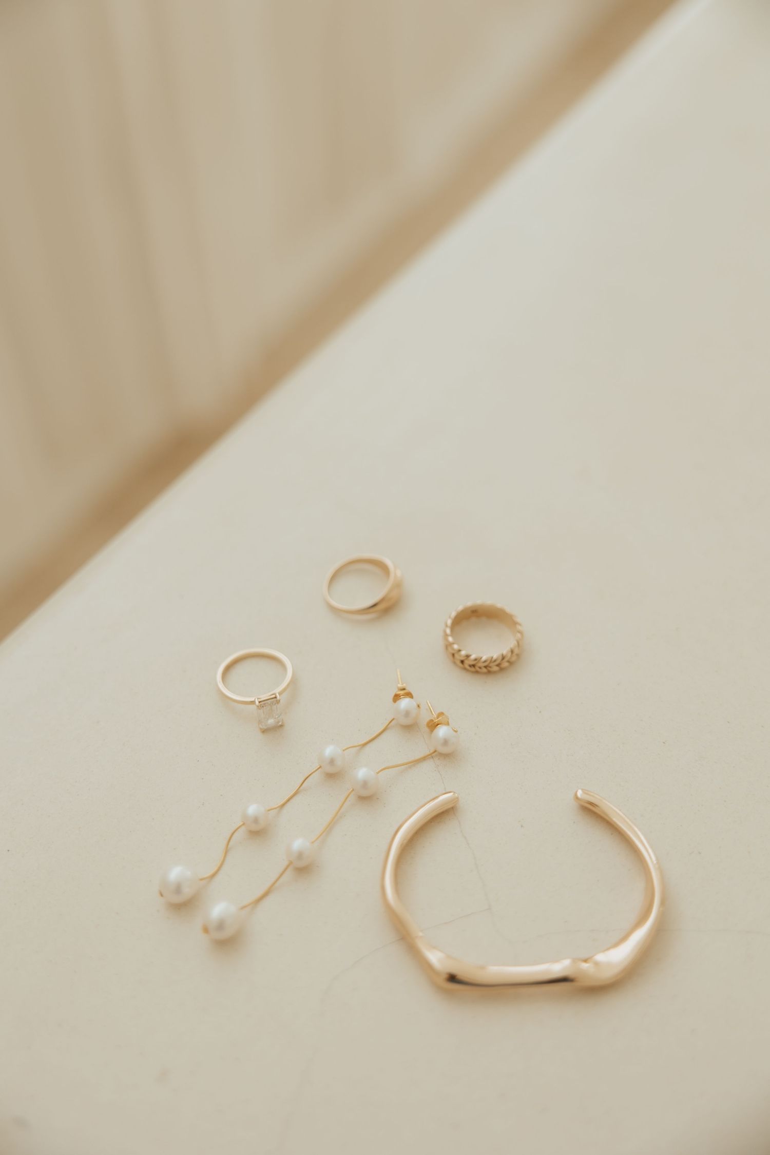 A collection of delicate gold jewelry pieces including rings, earrings and a bracelet arranged on cream fabric.