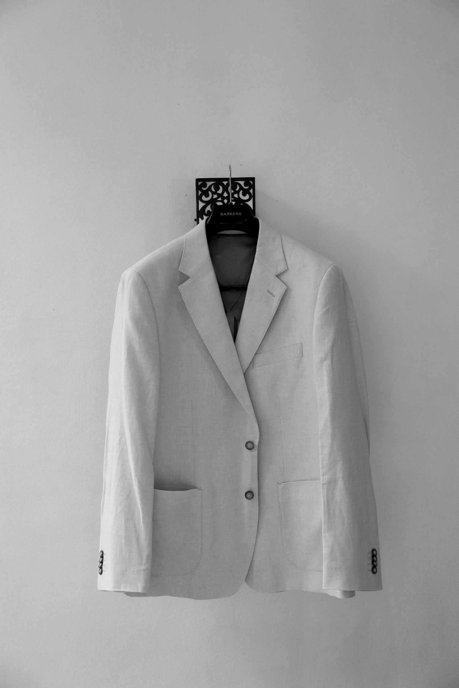 A crisp white suit jacket hanging on a decorative hanger against a light grey wall.