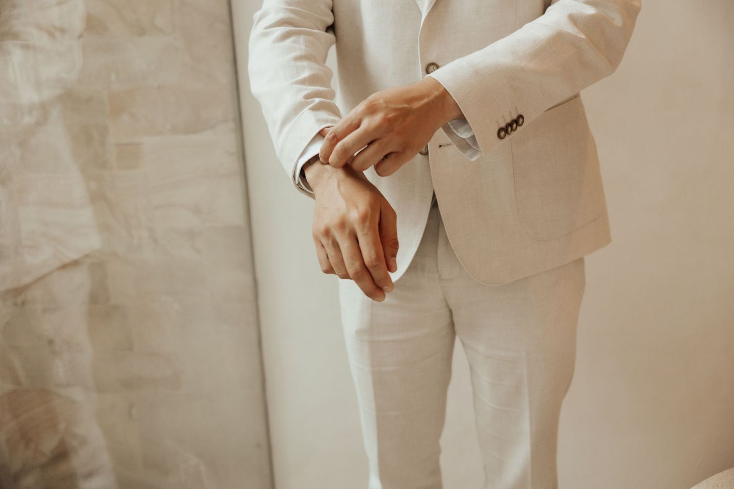 Close-up detail of hands checking a watch while wearing an elegant white suit and sleeve.