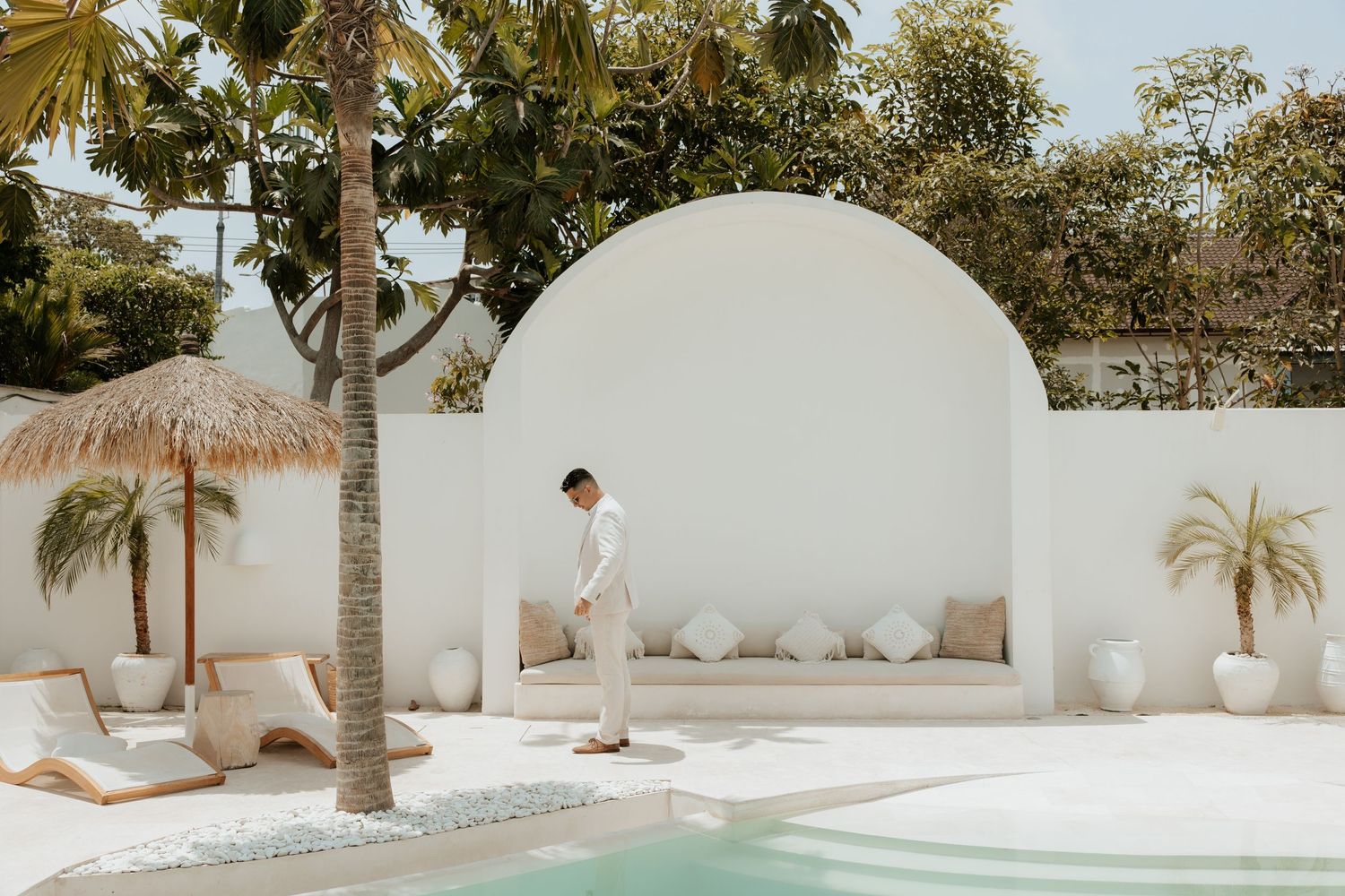 Modern white Mediterranean villa with curved archway, palm trees and swimming pool in a luxurious tropical setting.