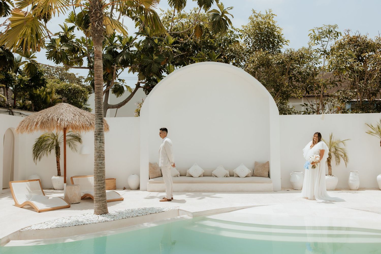 A white Mediterranean-style venue with arched walls and palm trees surrounding a swimming pool.