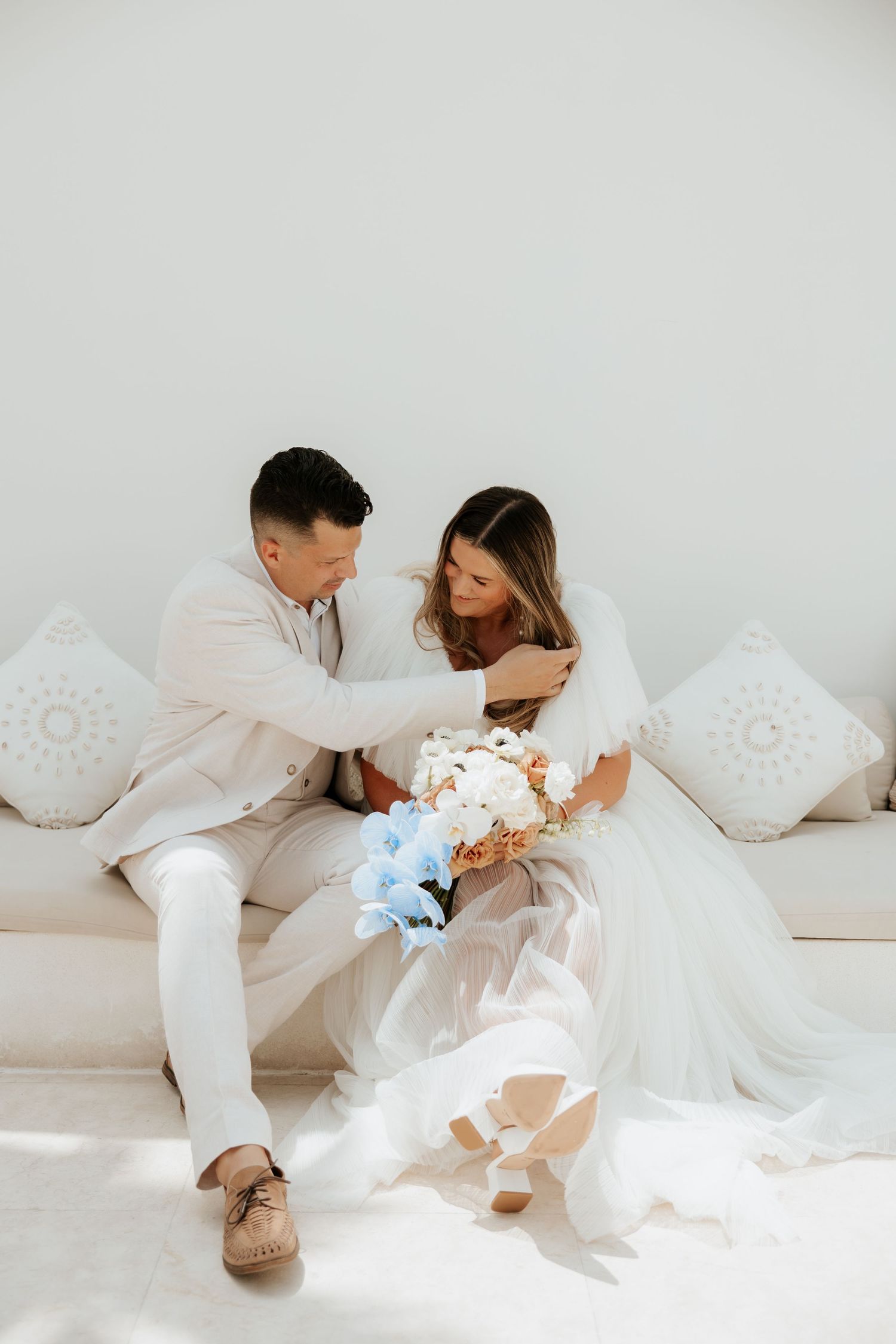 A romantic wedding moment captured on a white couch with decorative pillows.