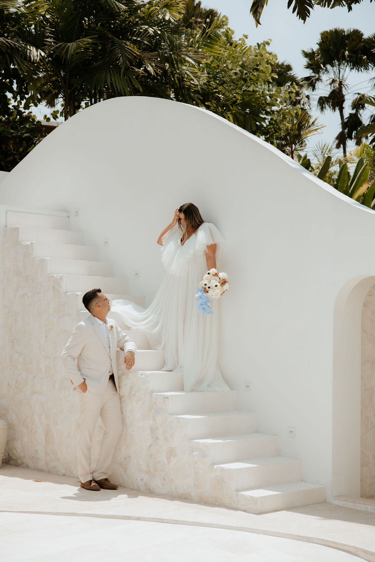 A wedding photo on white Mediterranean steps with a couple in white attire and a bouquet.