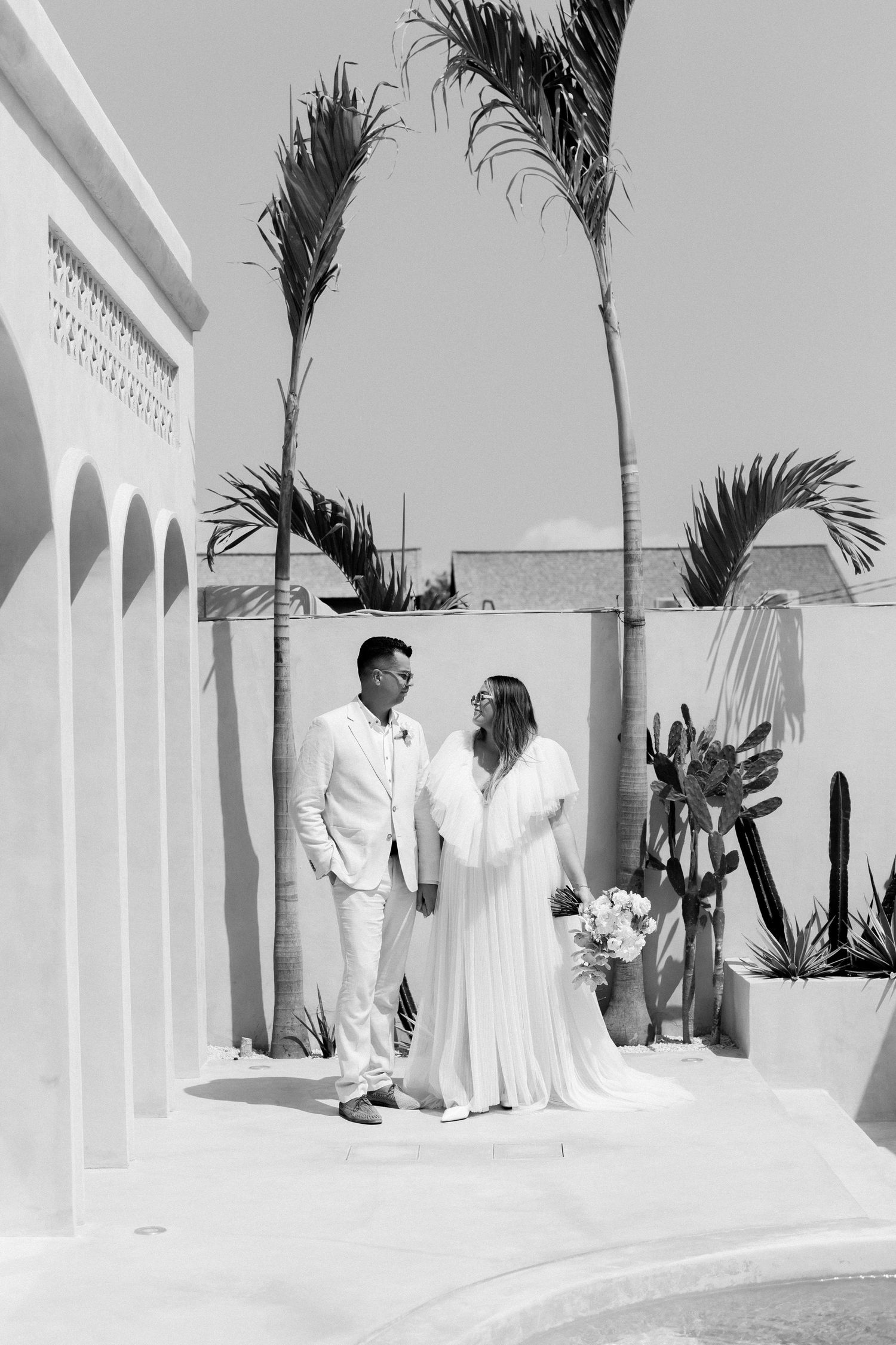 Black and white wedding photo with palm trees and white architectural details.