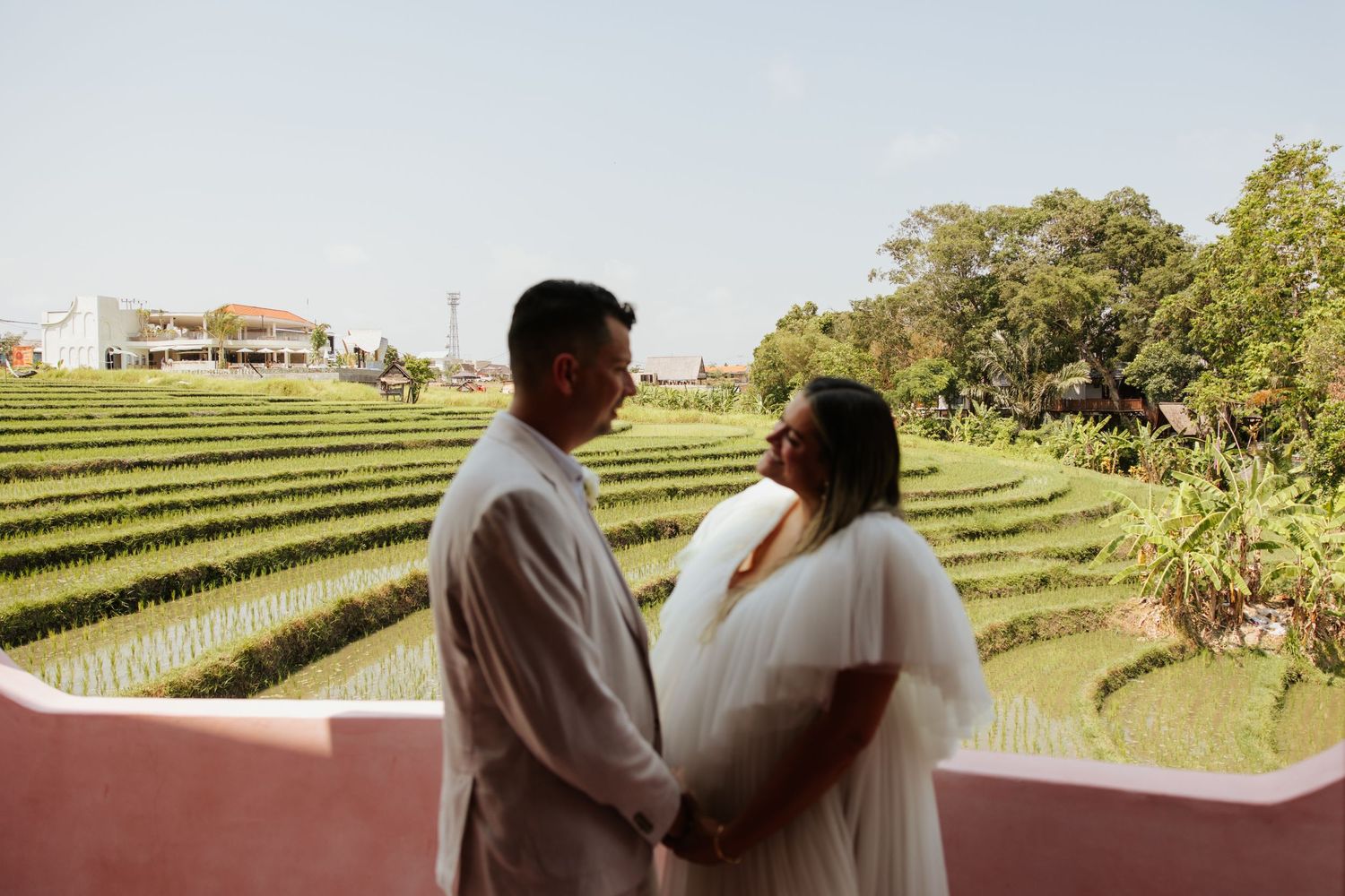 A loving couple holds hands while overlooking lush green terraced rice fields on a sunny day.