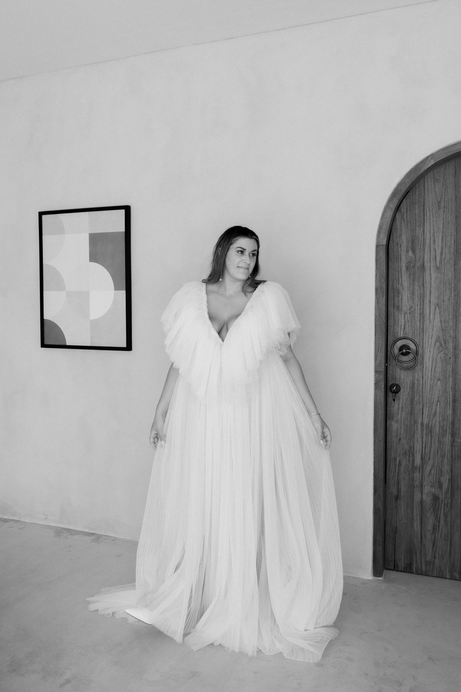 Bride wearing dramatic white tulle wedding gown posing in minimalist interior.