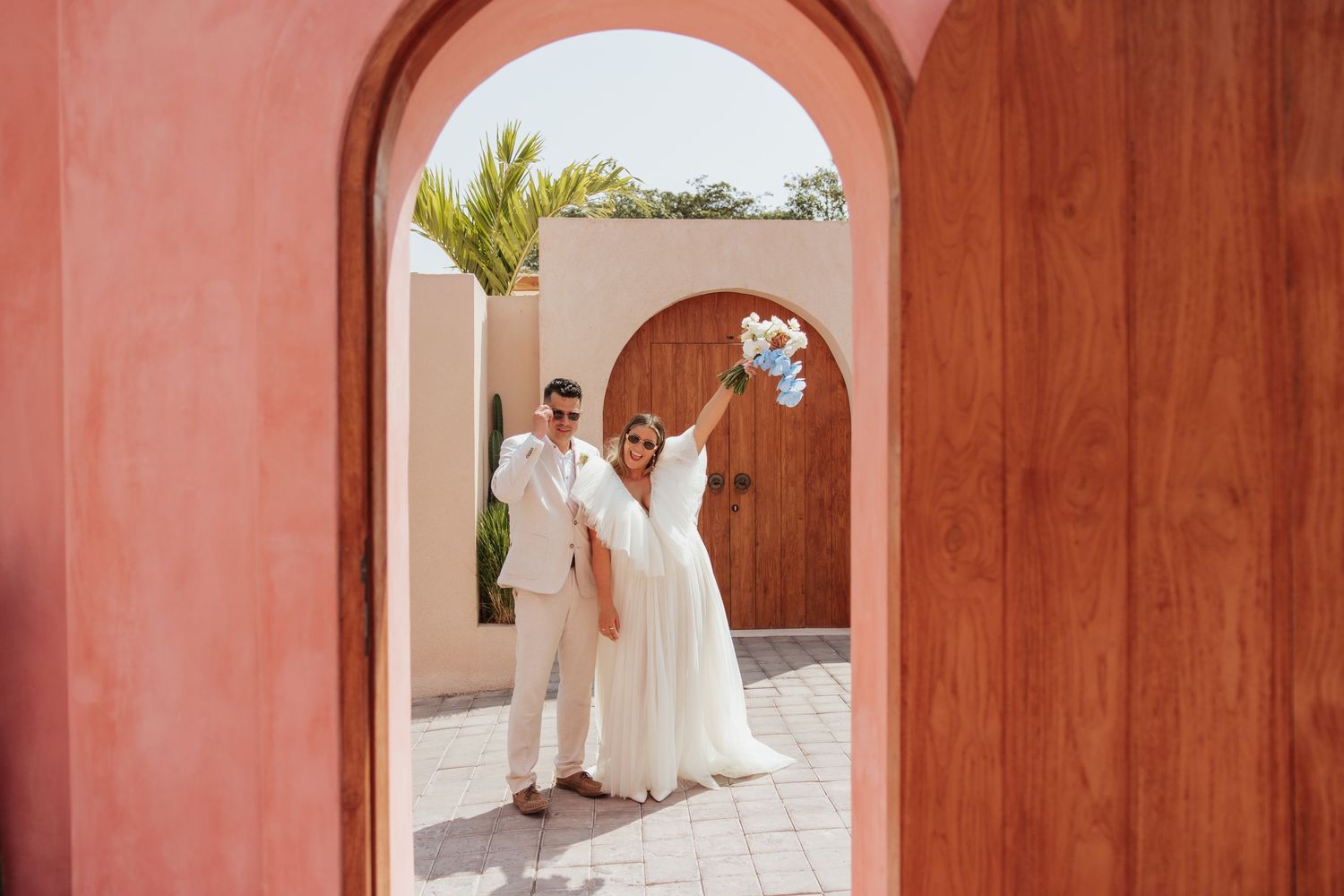 Wedding couple framed through a terracotta archway in a Mediterranean-style setting.