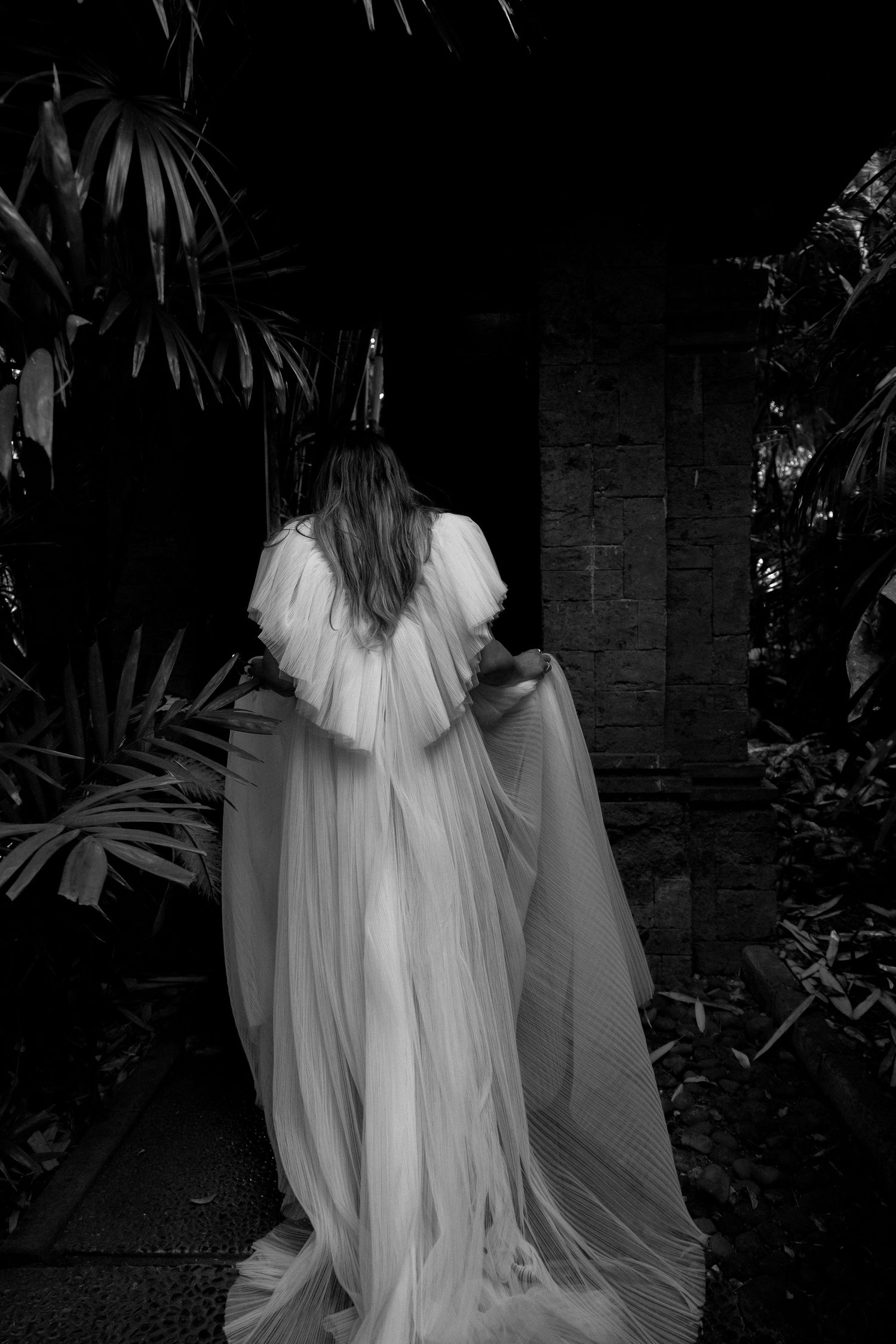 Black and white photo of a wedding dress with dramatic flowing veil and ruffled details.