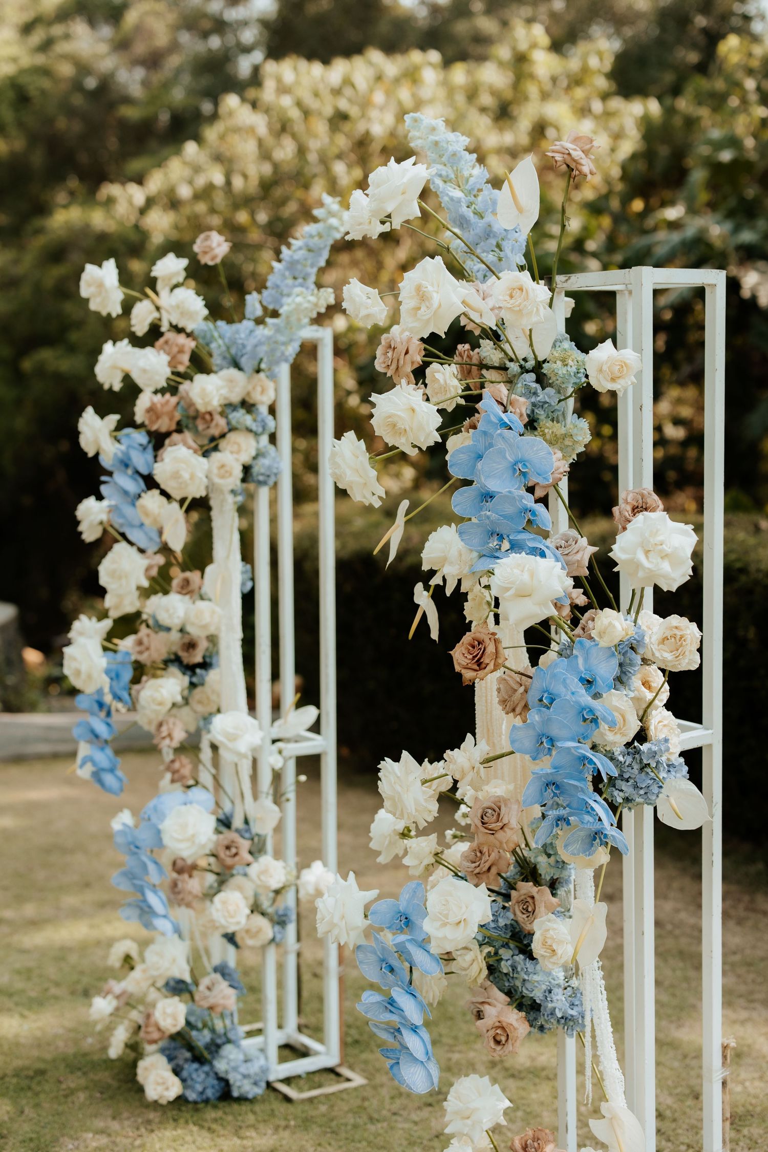 A stunning floral arch with blue and white flowers decorates an outdoor wedding setup.