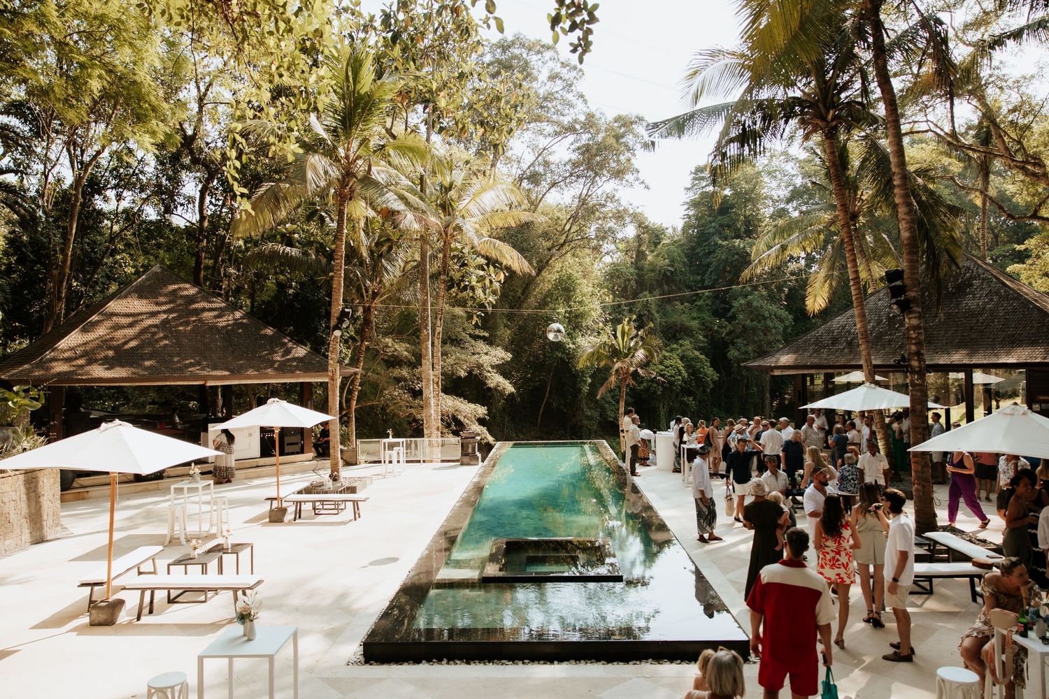 Tropical wedding venue with modern infinity pool and outdoor seating under palm trees.