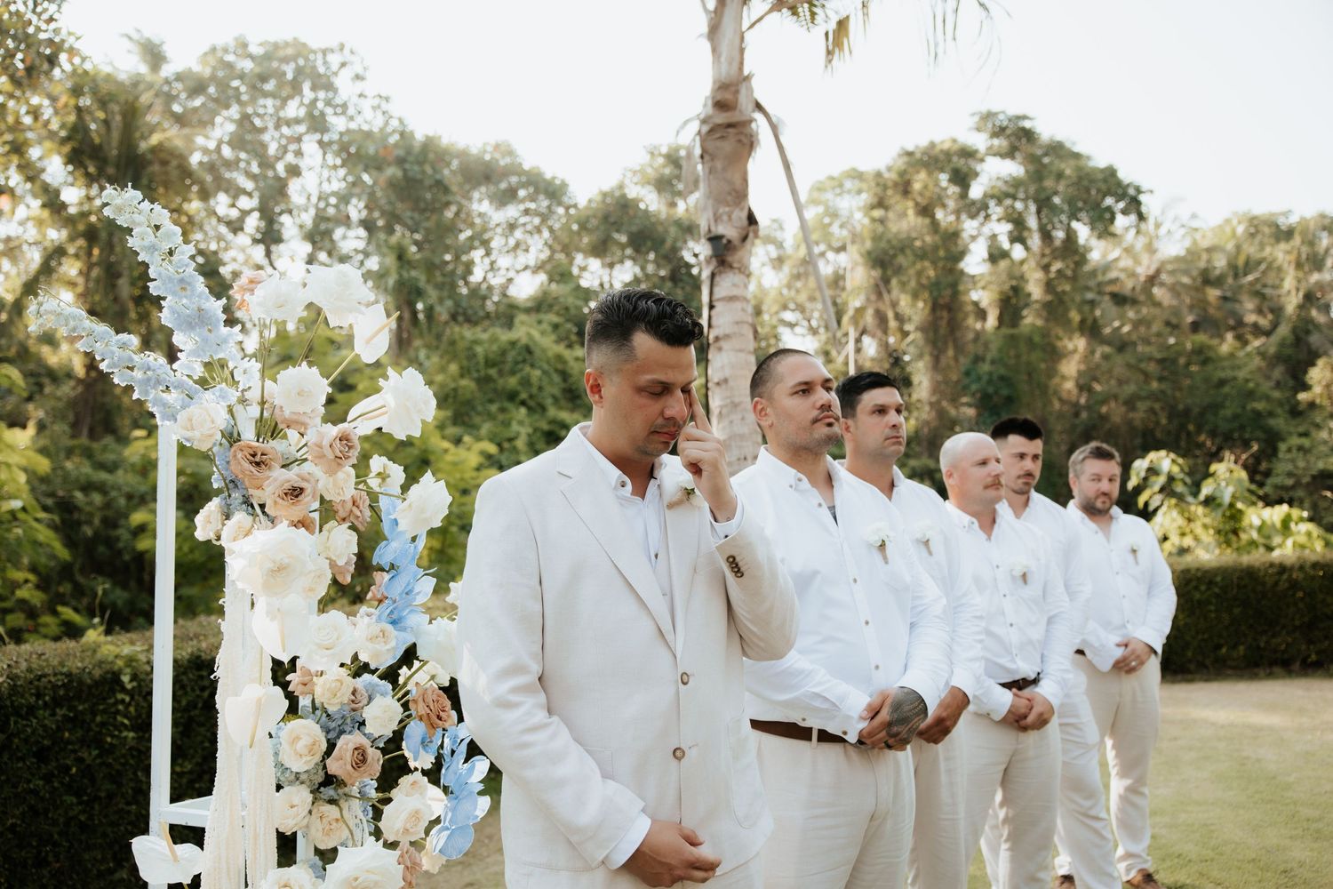 A wedding ceremony setup with white decor and floral arrangements in a tropical garden setting.