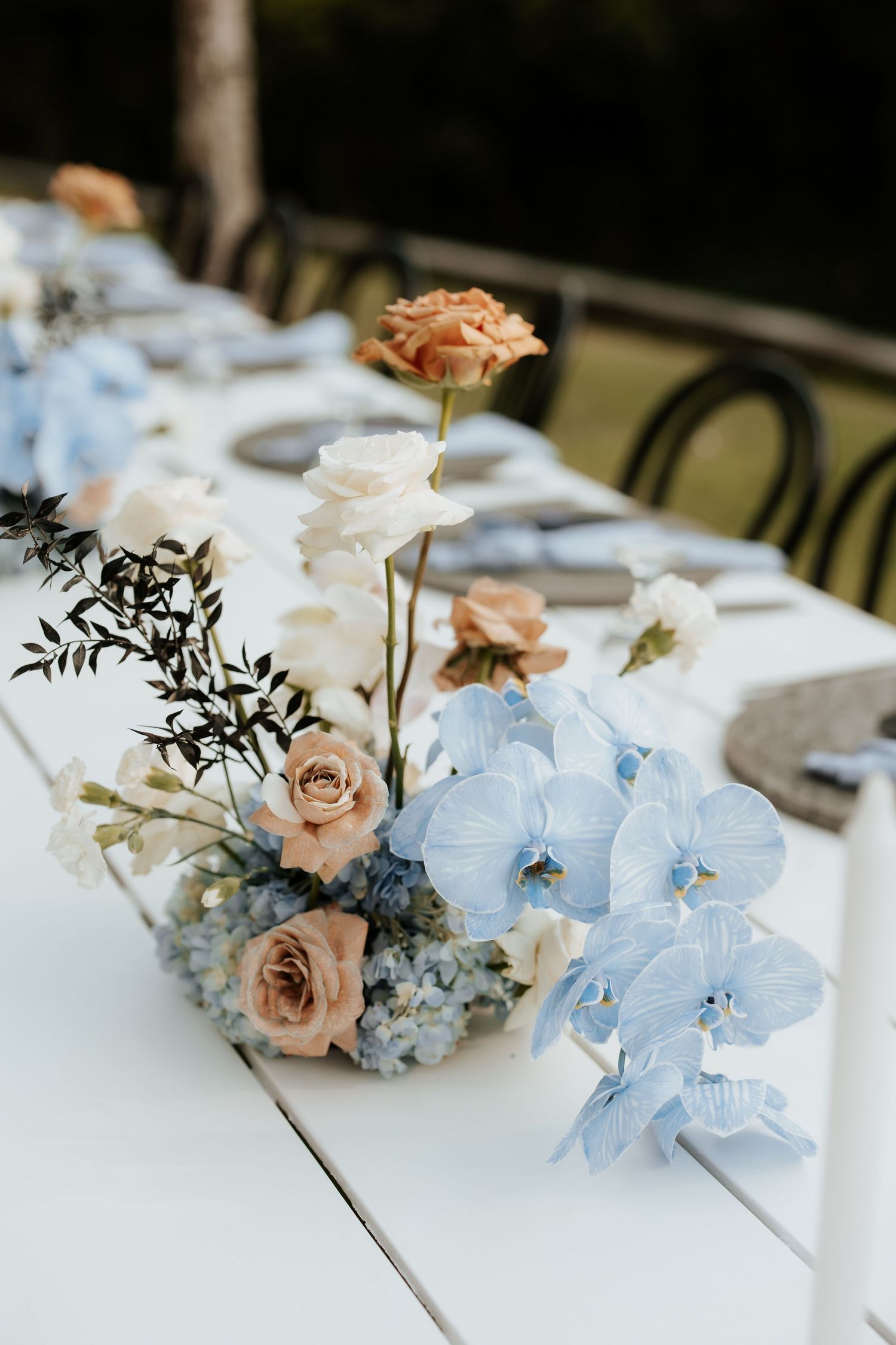 Elegant table centerpiece featuring blush roses and light blue orchids on a white tablecloth.