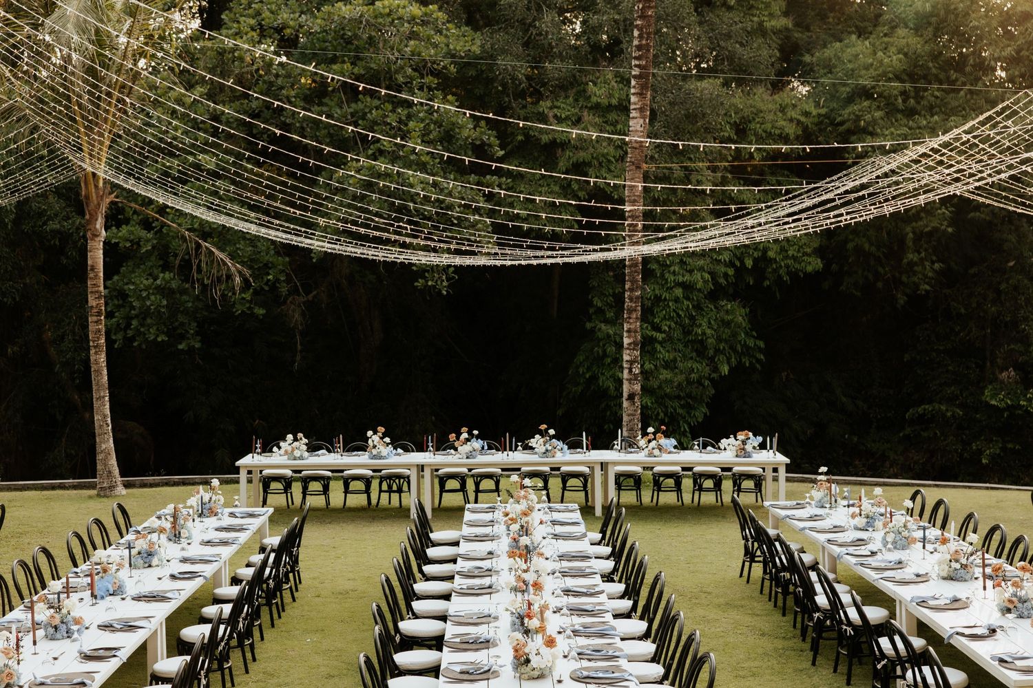 Long dining tables set under string lights for an outdoor wedding reception.