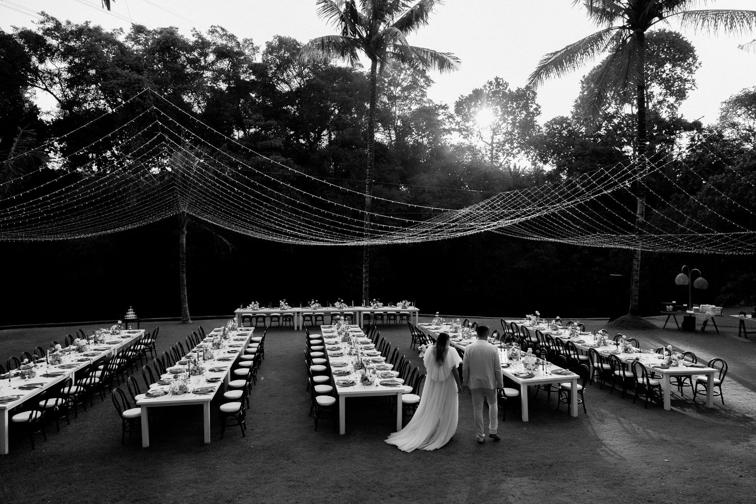 Black and white photo of wedding reception setup with long tables under string lights.
