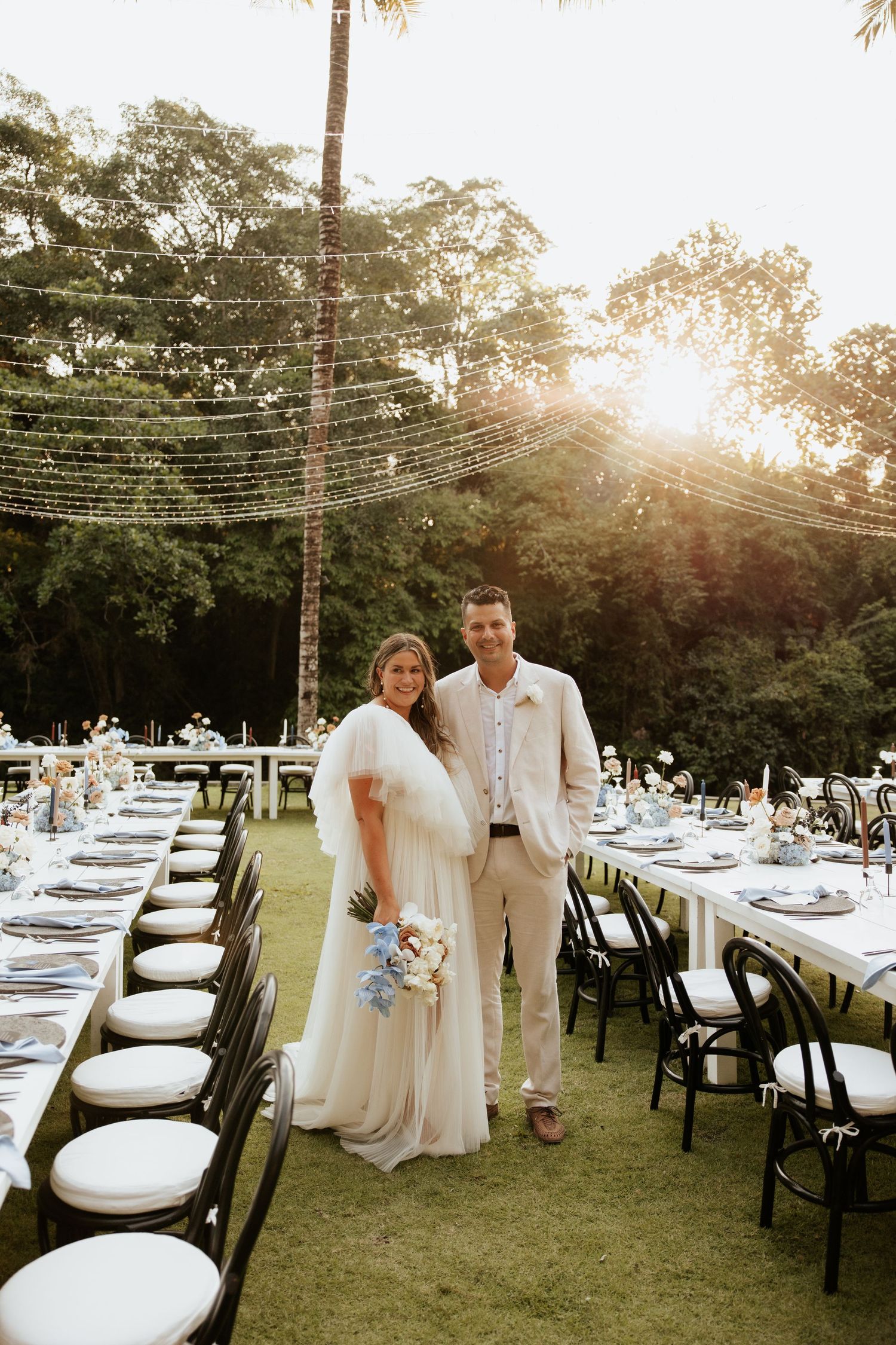 A couple stands between elegant table settings at their outdoor wedding reception.