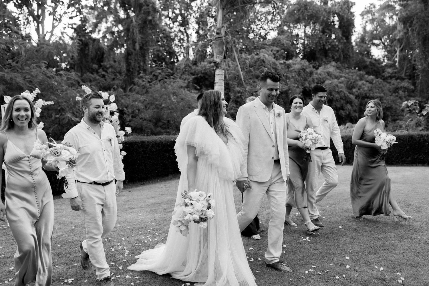 Black and white photo of wedding party walking through a garden setting.