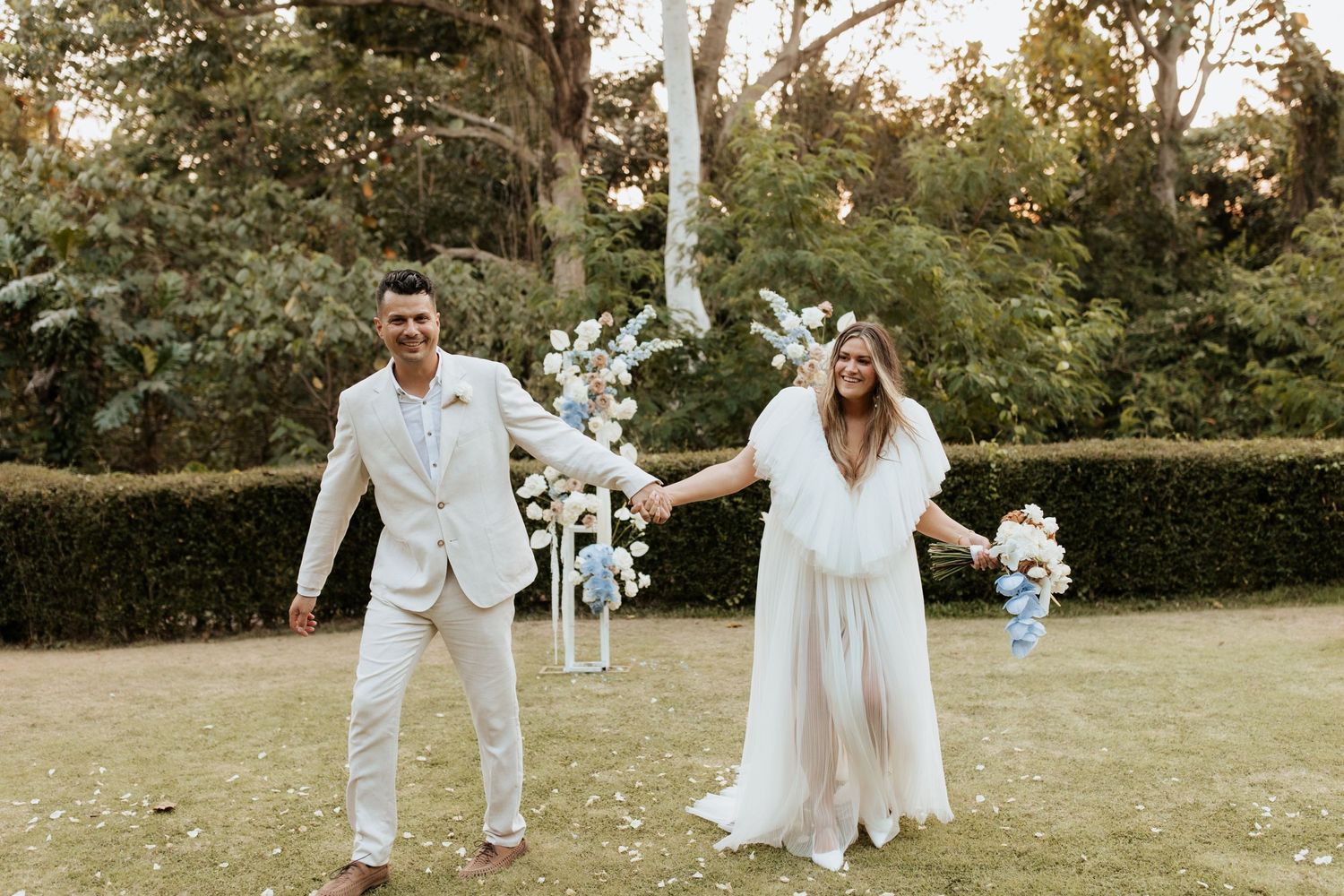 A joyful couple celebrates under a floral arch decorated with blue and white flowers.