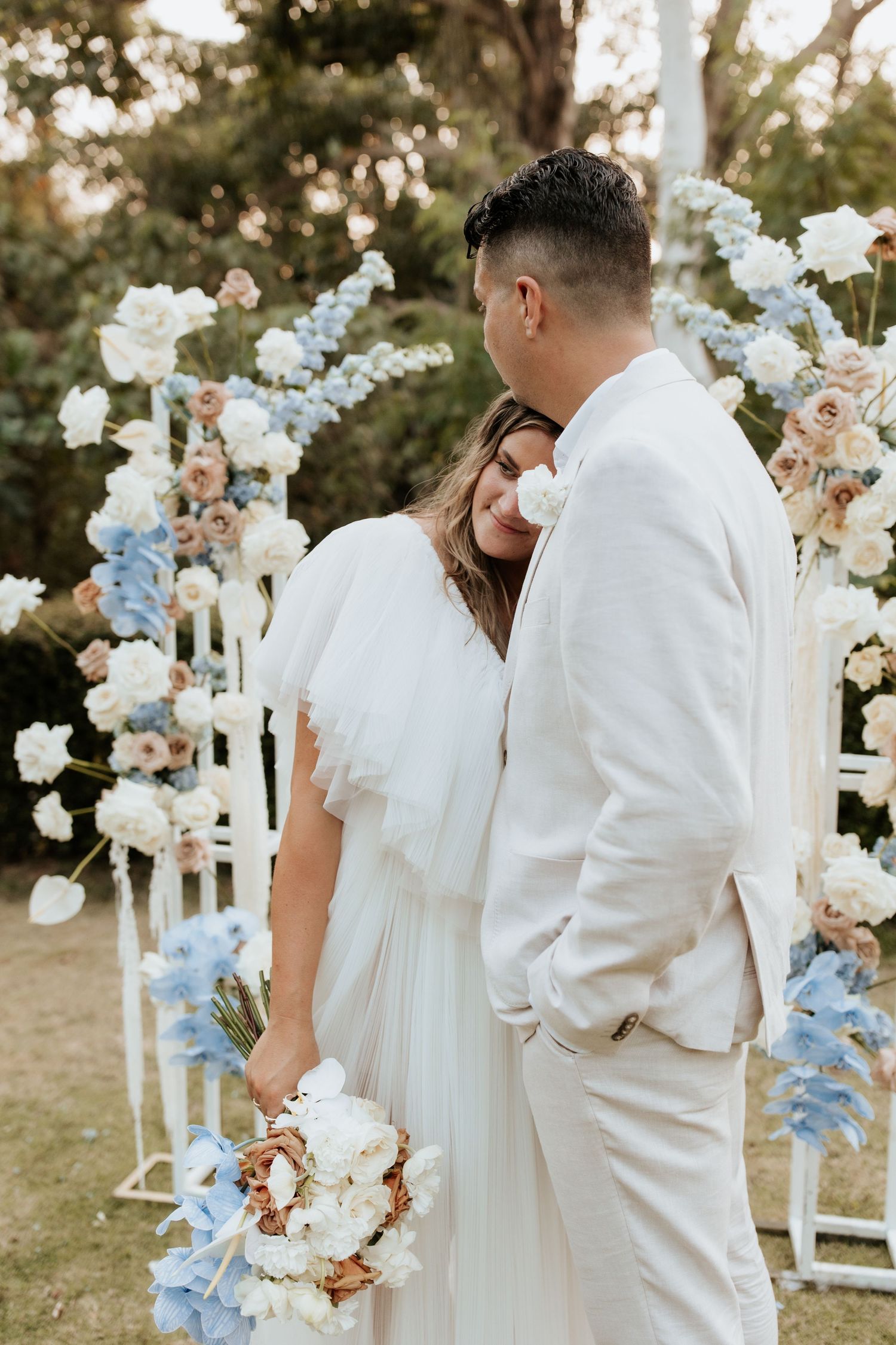 Wedding couple embracing near floral arch with white and blue flowers.