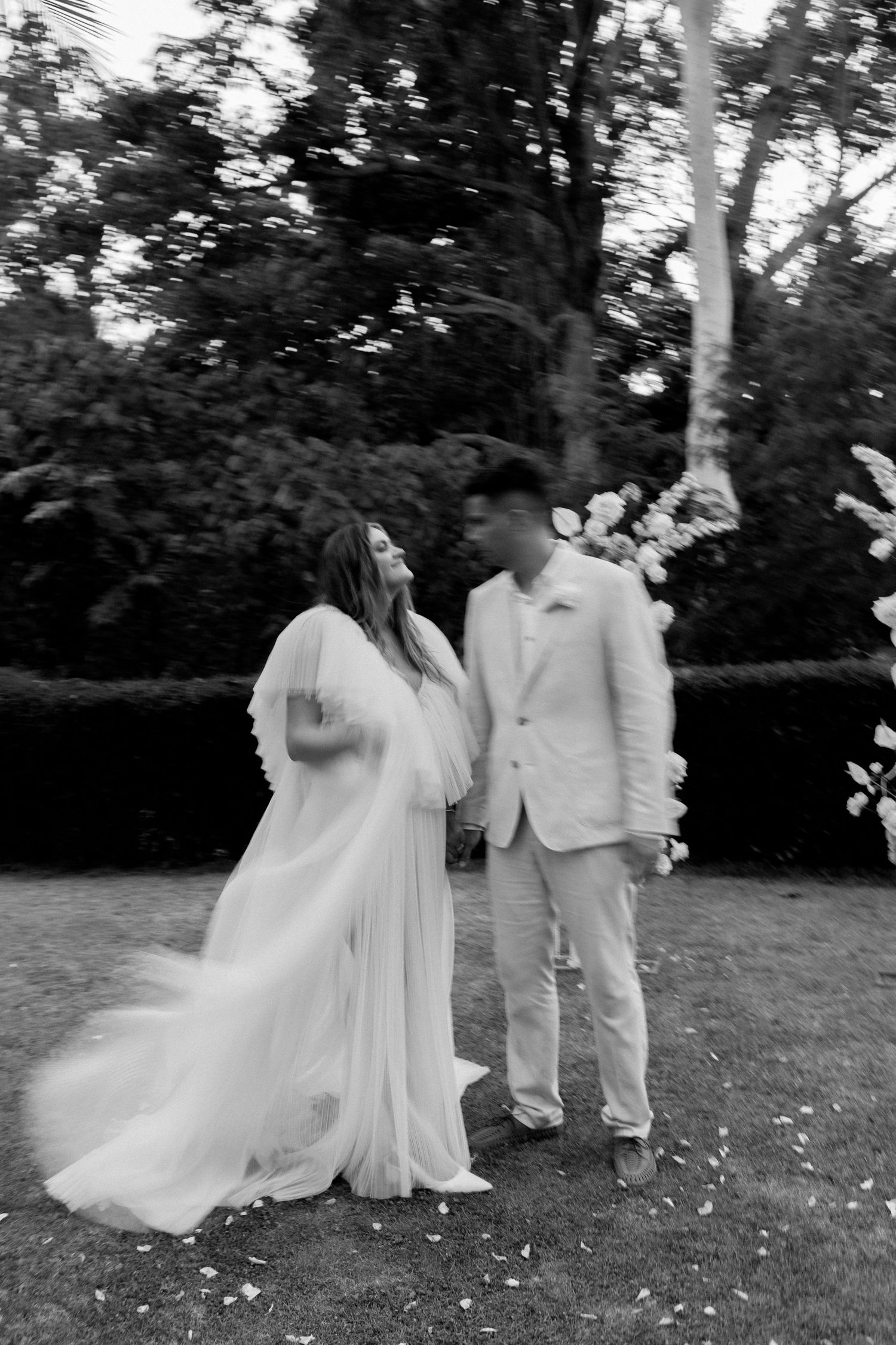 Black and white photo of a couple in wedding attire standing in a garden setting.