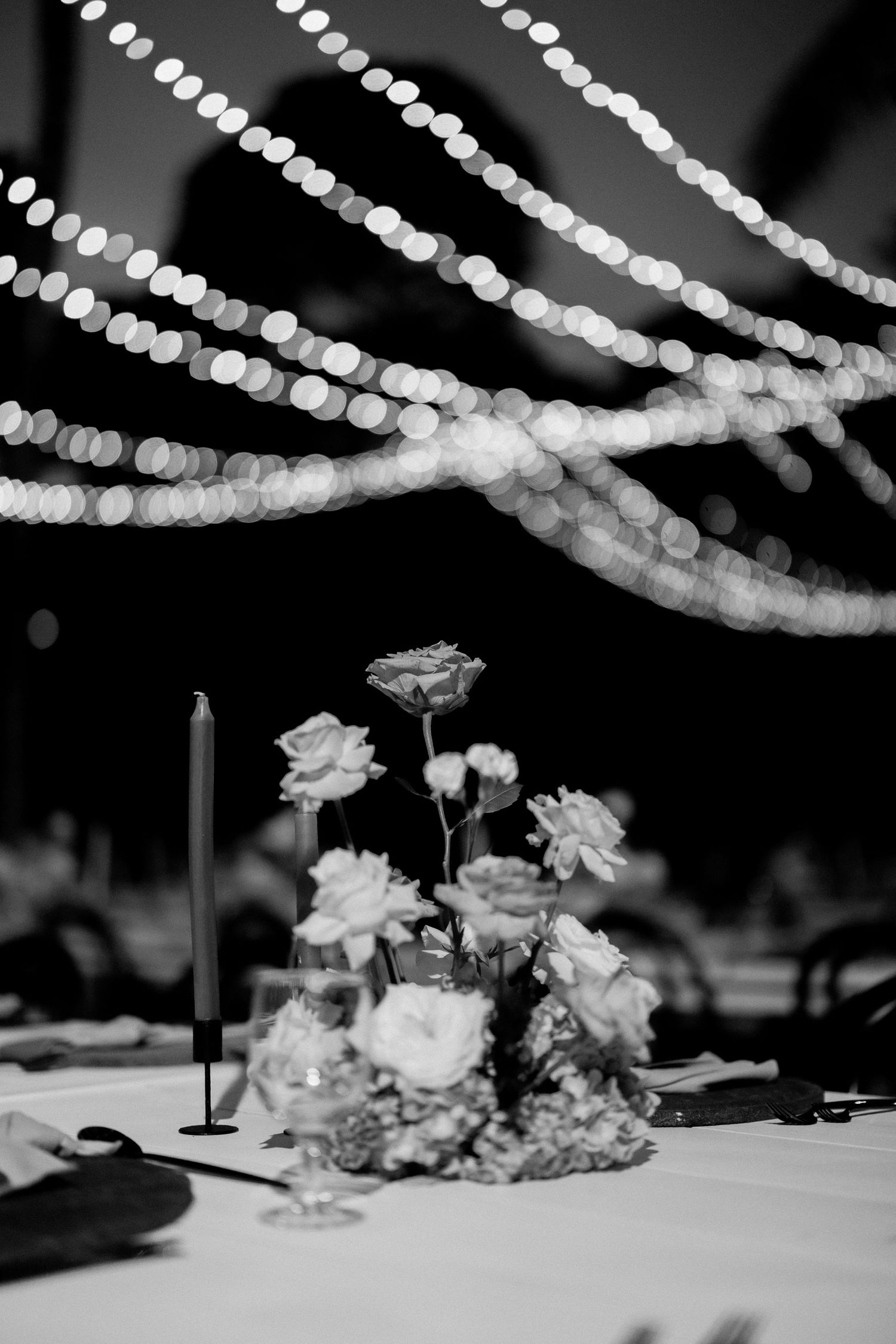 Black and white wedding reception table setting with string lights and floral centerpiece.