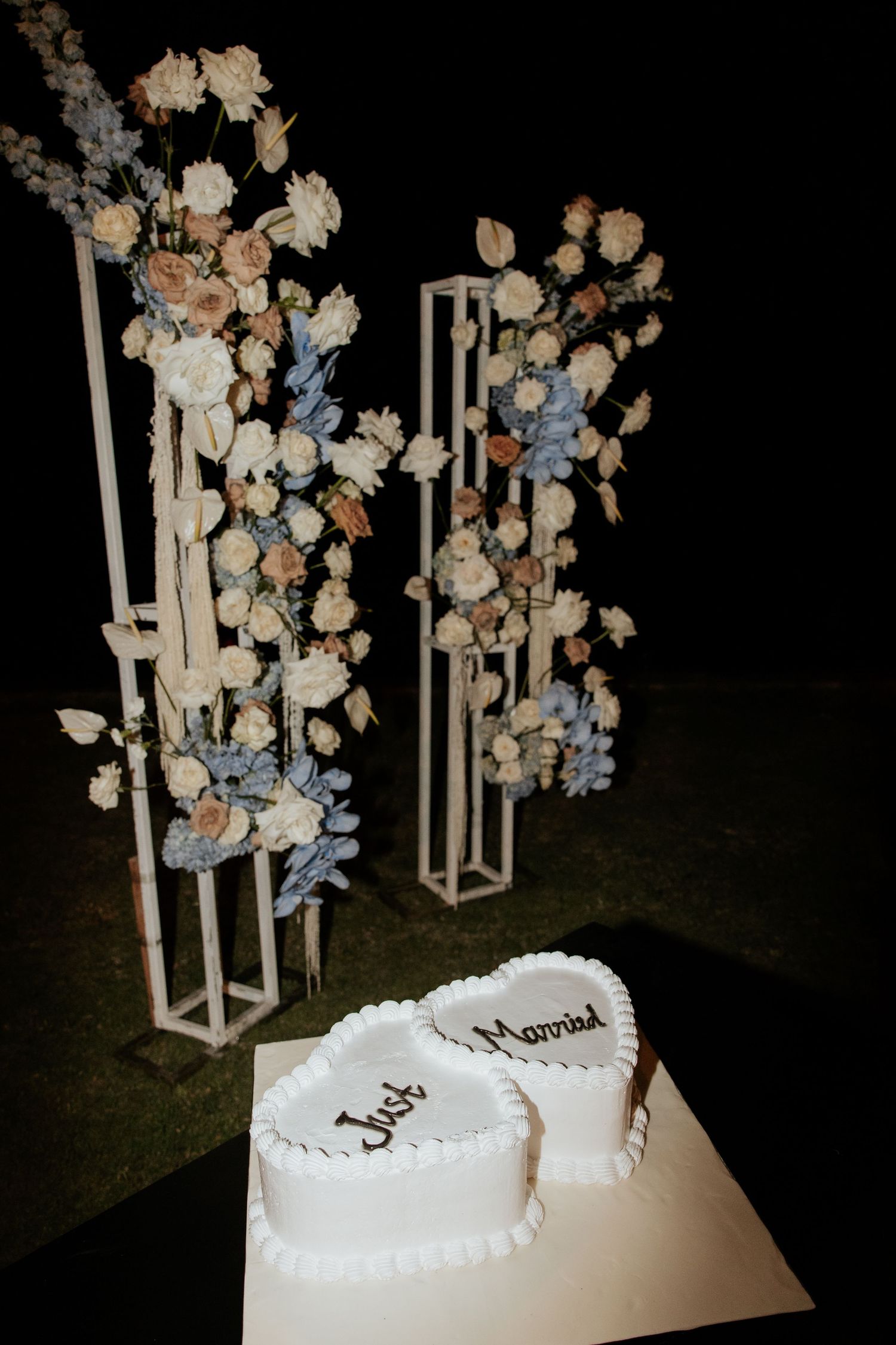 Elegant wedding decoration featuring white floral stands and a heart-shaped white wedding cake.