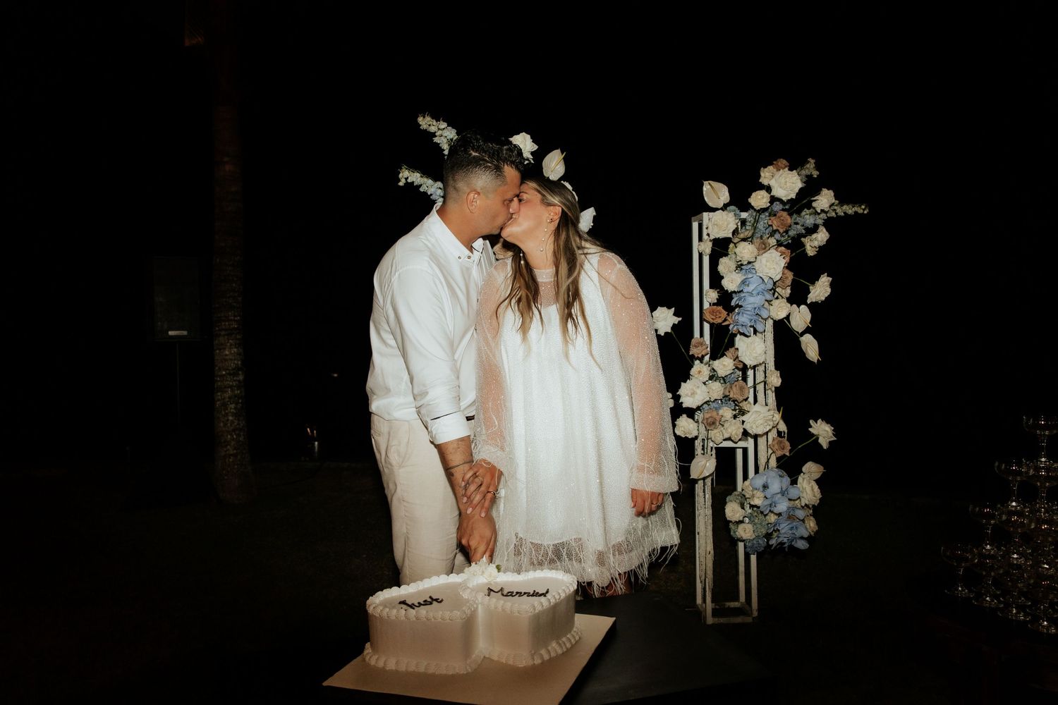 A couple shares an intimate moment at their wedding cake table decorated with elegant white floral arrangements.