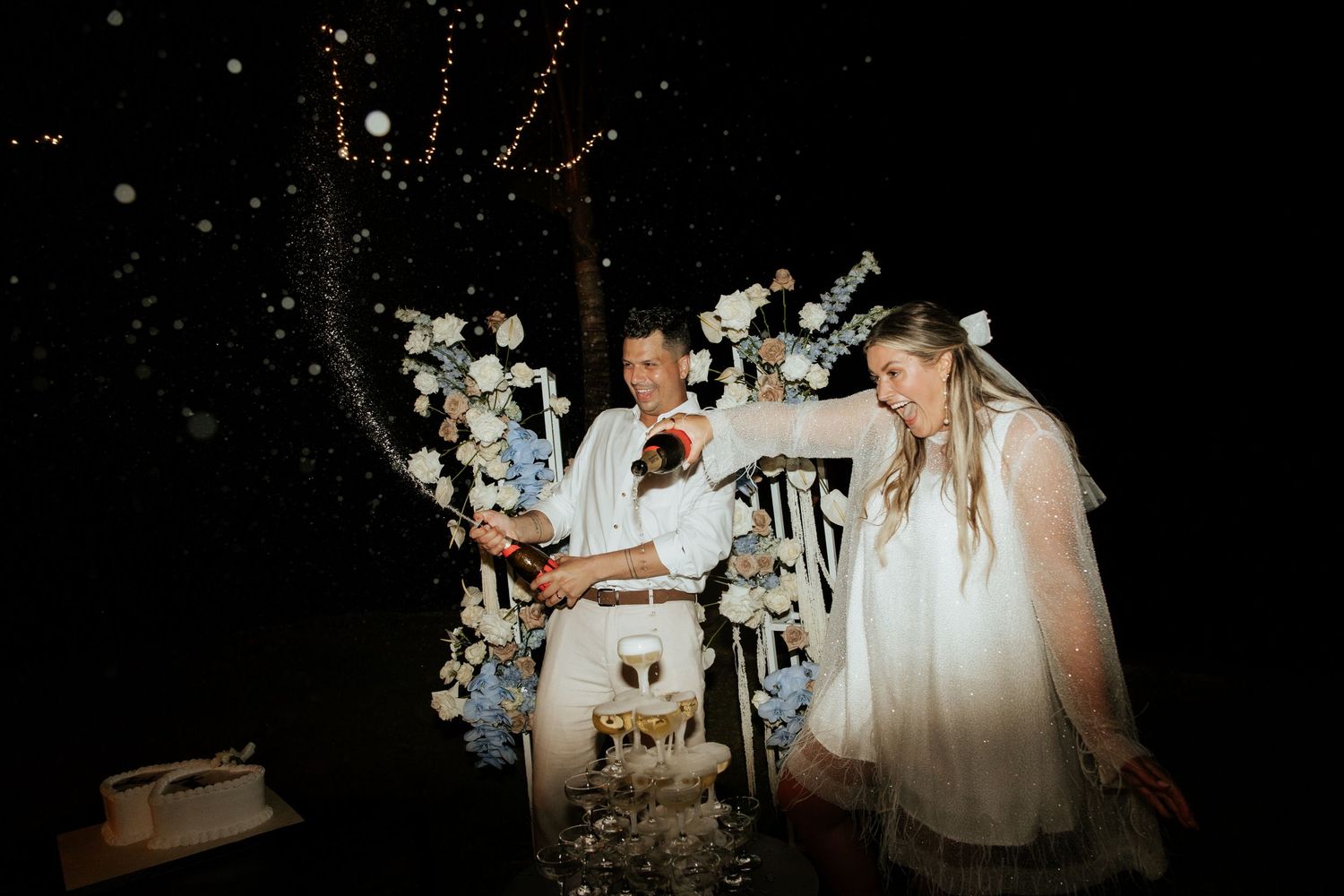 Guests spray champagne in celebration at an outdoor nighttime wedding reception.