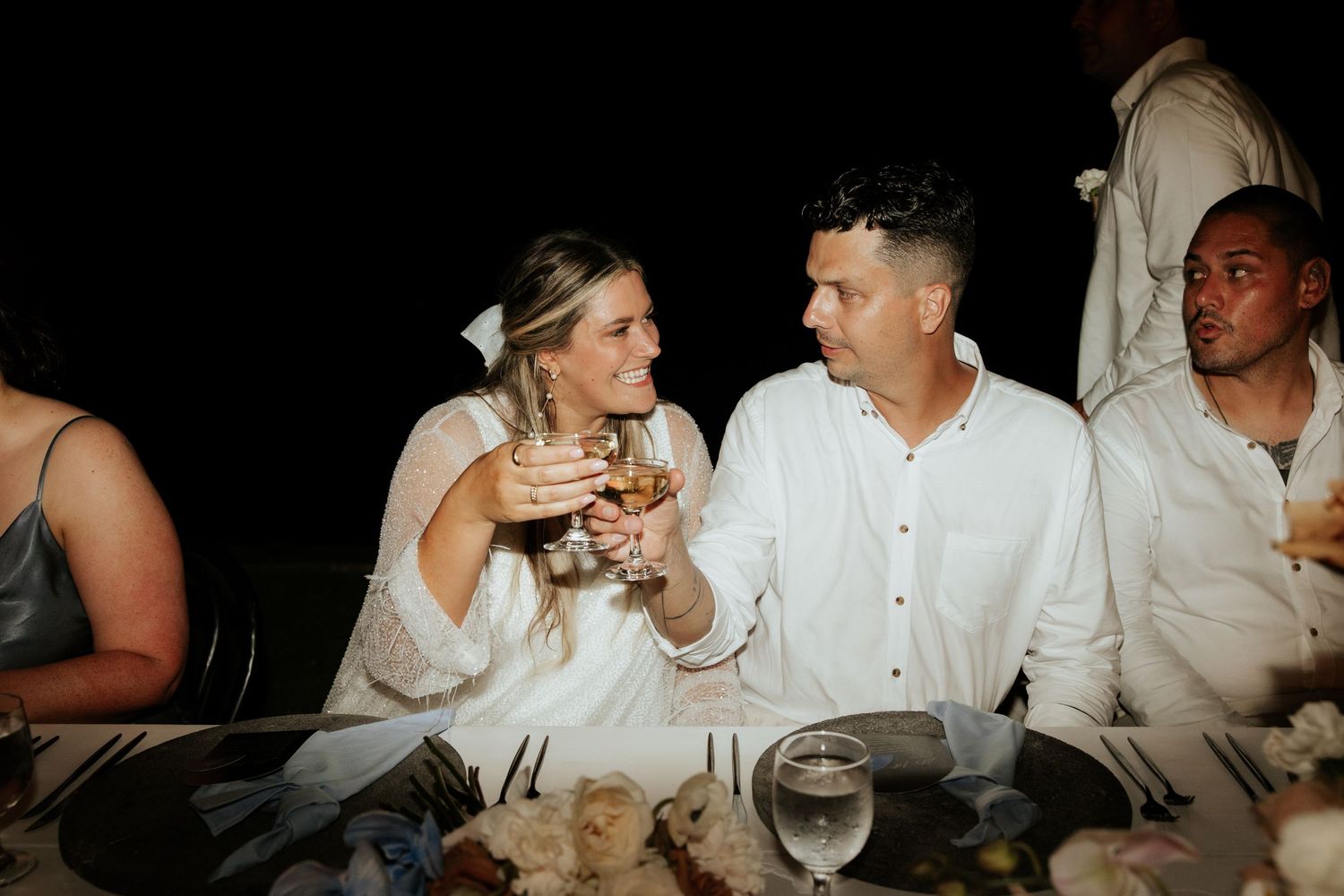 Wedding party enjoying drinks and conversation at an outdoor reception table.