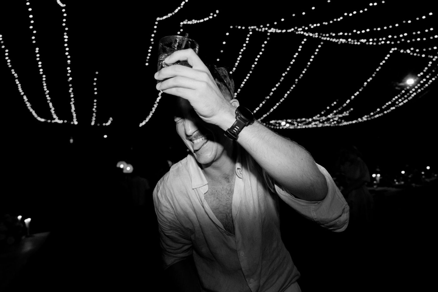 Person dancing under twinkling string lights at an outdoor nighttime celebration.