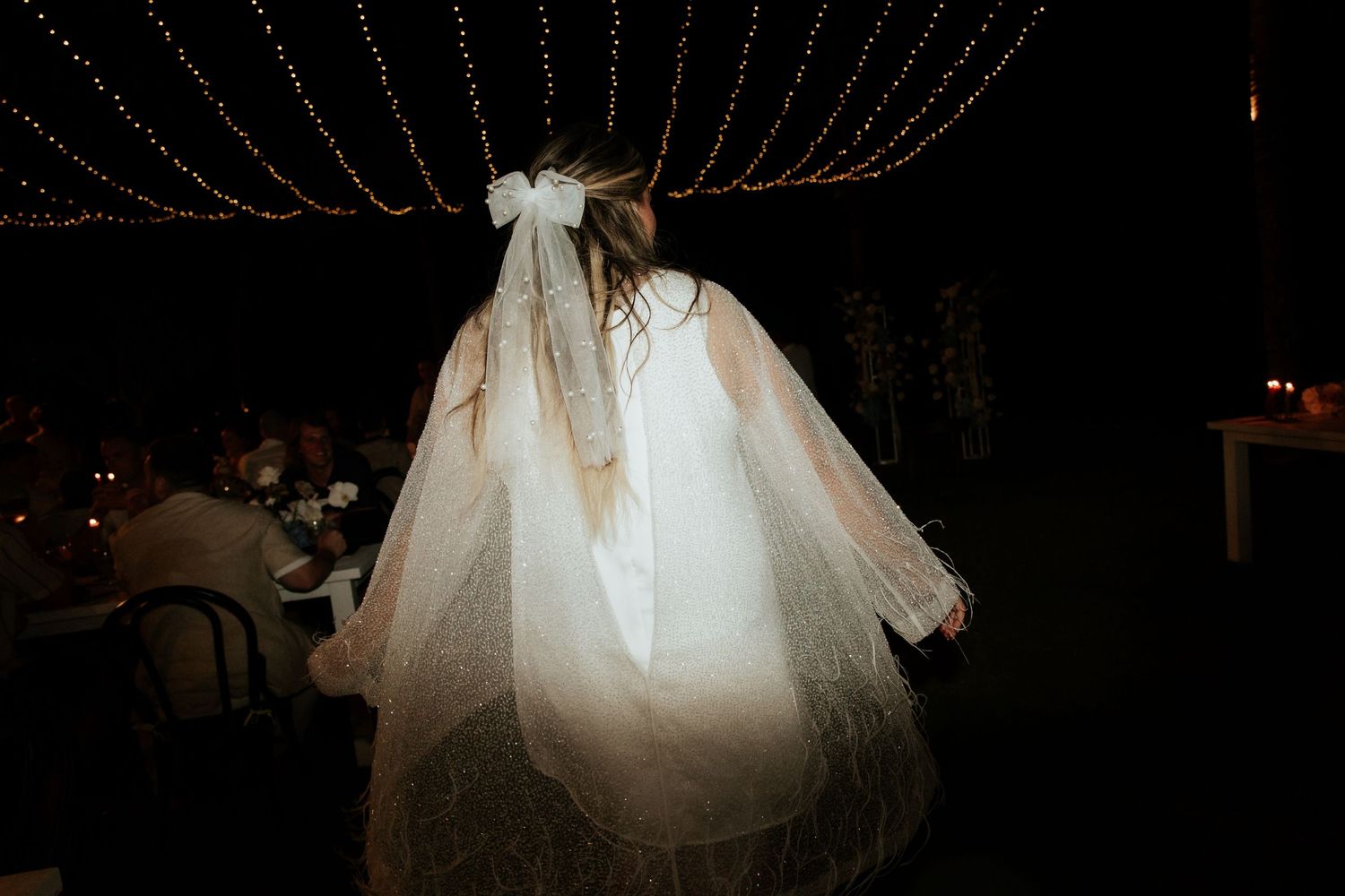 Back view of a wedding dress glowing ethereally under romantic string light decorations at night.