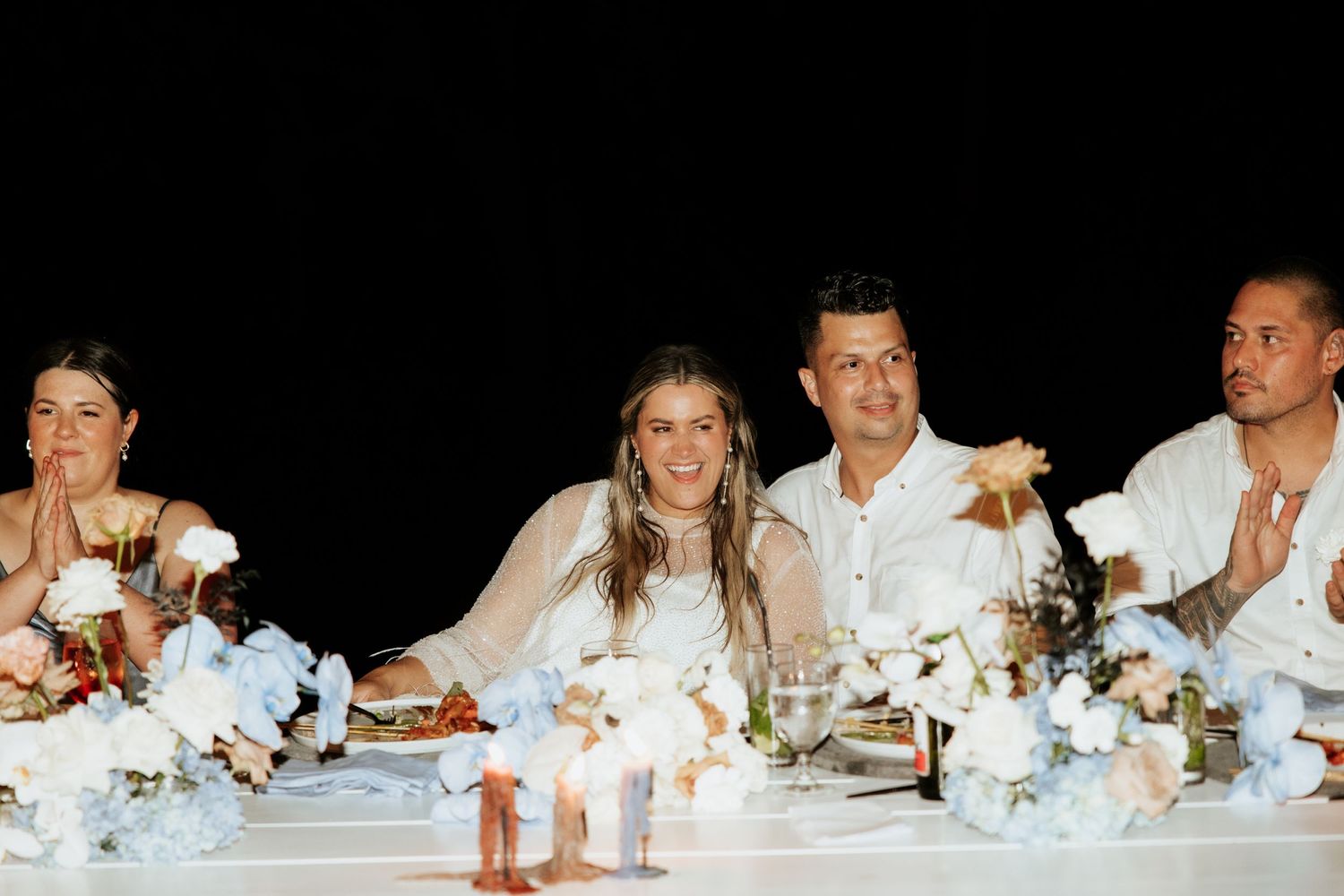 Wedding party seated at the head table with blue and white floral decorations during the reception.