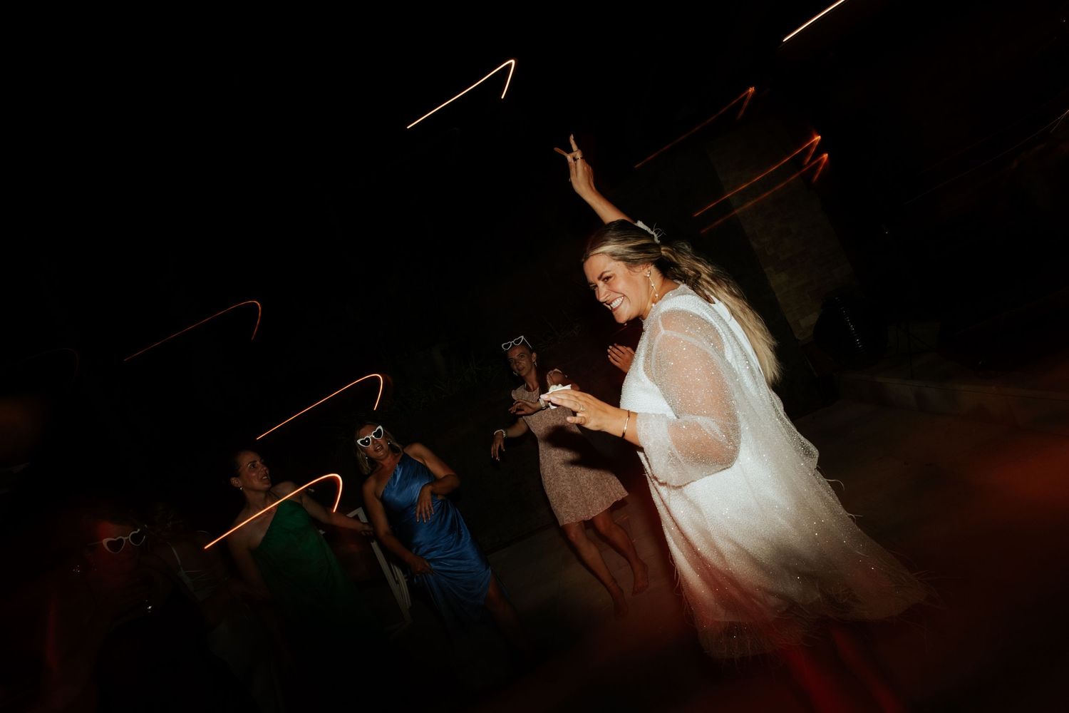 Dancing figures silhouetted against a dark background at a wedding reception.