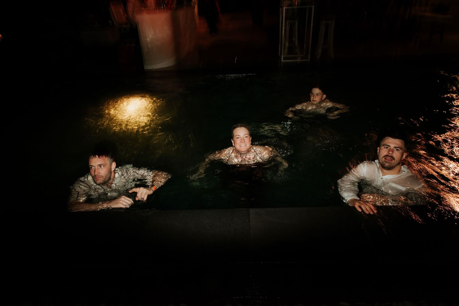 Group enjoying a nighttime swim in a dimly lit pool during a celebration.