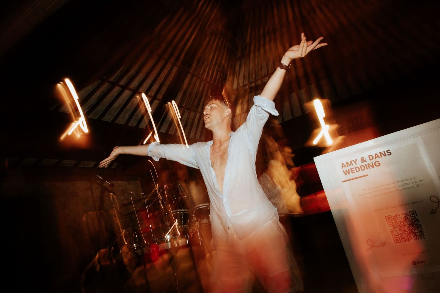 A performer in white raises their arms dramatically on stage with atmospheric lighting creating a dynamic silhouette.