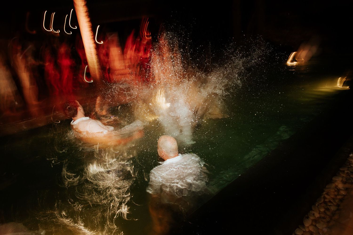 Splash effect in illuminated swimming pool creating dramatic water patterns at night.