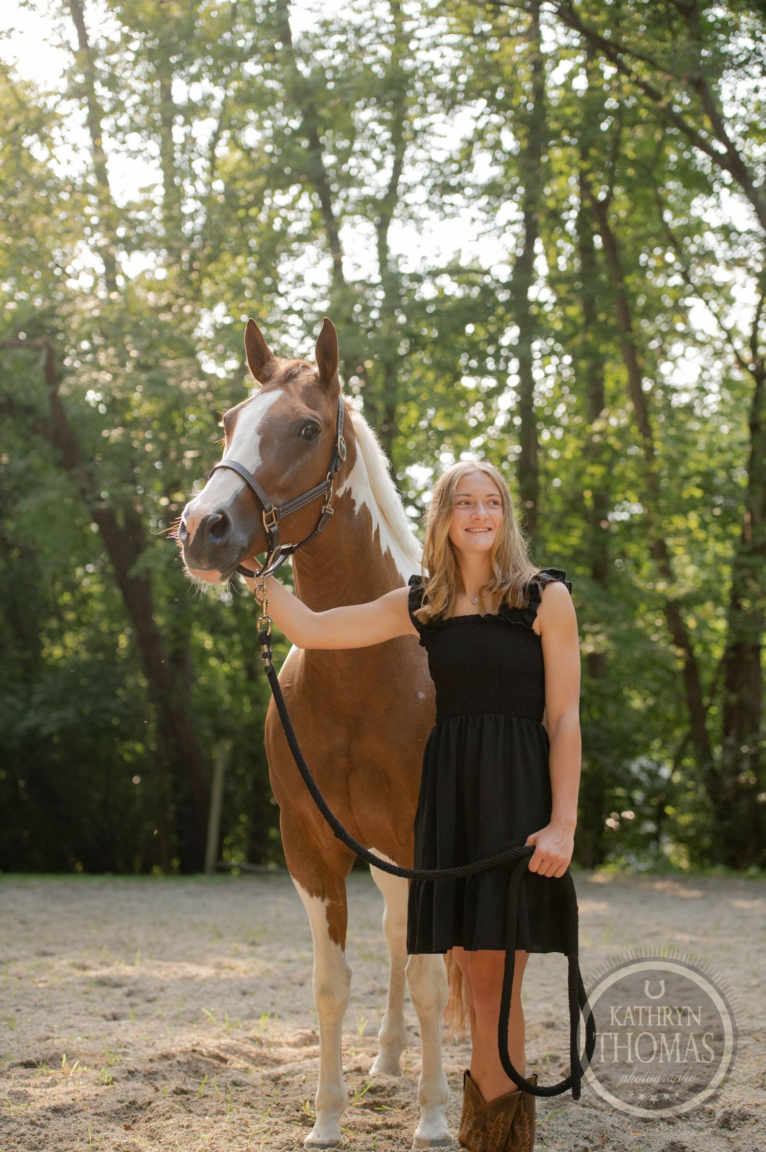 Chestnut horse with white markings posed next to person in black dress outdoors.