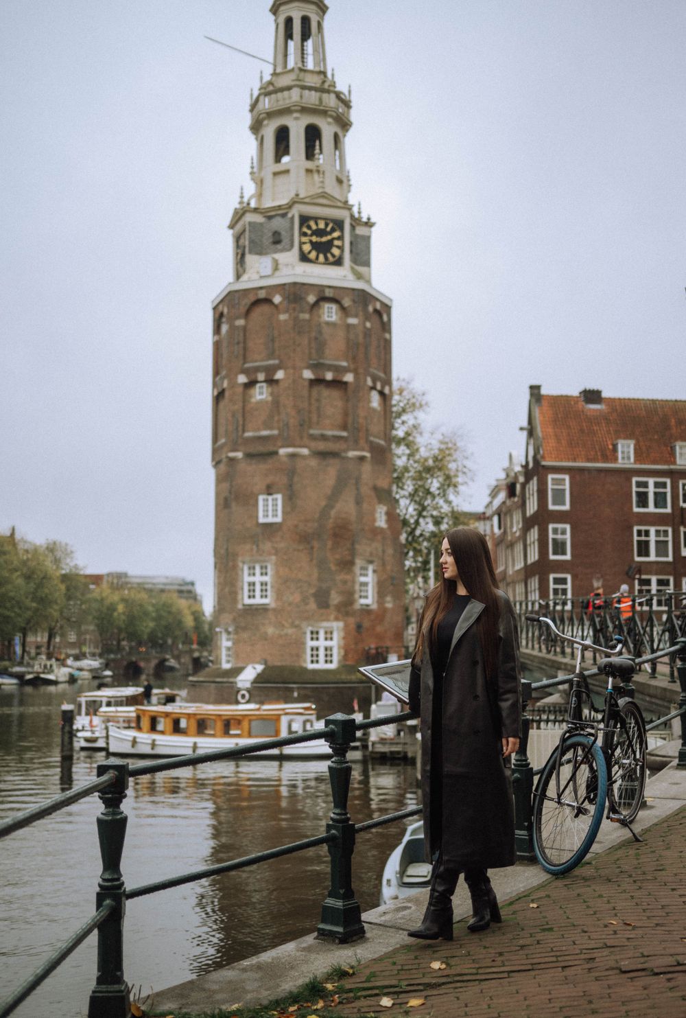 Person walking along canal path with historic Dutch architecture and boats in background.