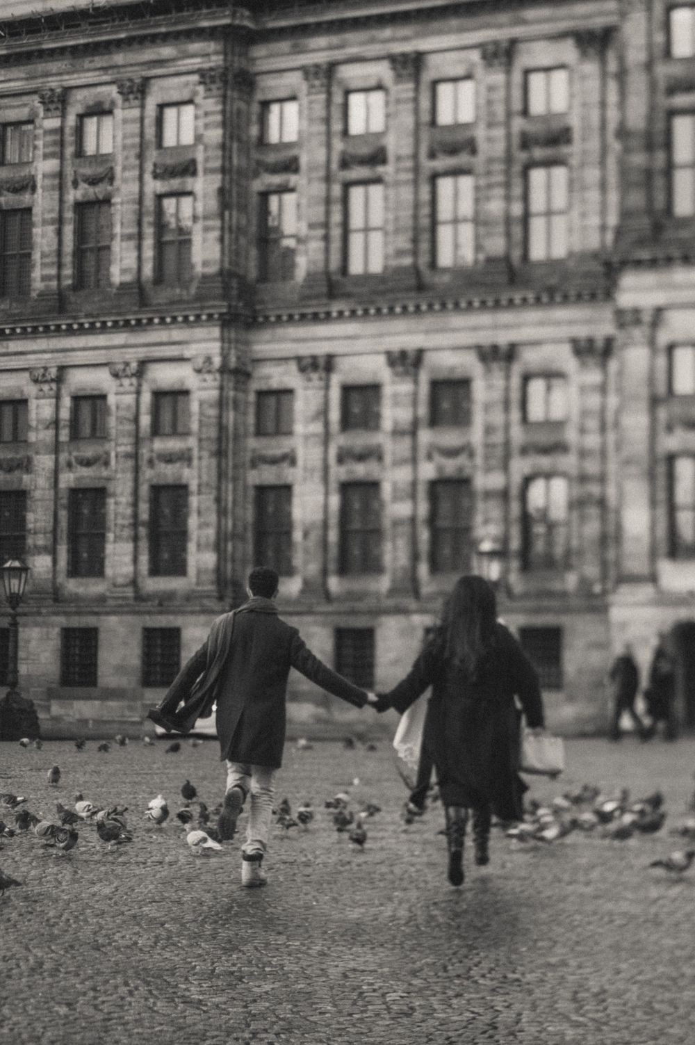 People walking across cobblestone square in front of grand historic building.
