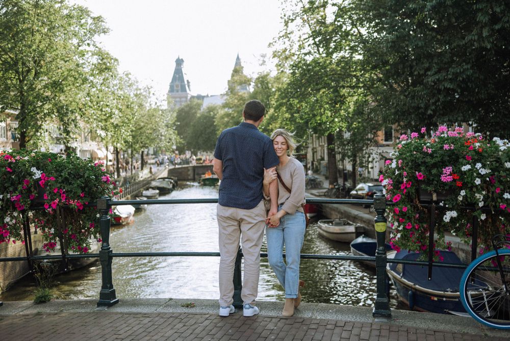 A romantic stroll along Amsterdam's canal with blooming flowers and boats in the background.