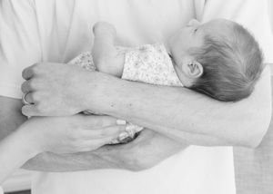 Tender in-home newborn session, baby laying peacefully in parents’ arms, natural window light.