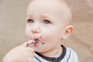 Messy milestone moment, baby’s cheeks and nose covered in frosting, laughing joyfully.