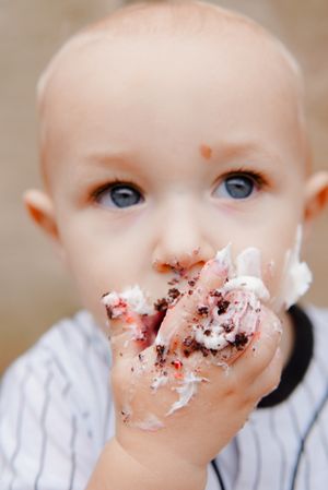 Playful smash cake moment, baby covered in frosting, smiling with messy fingers.
