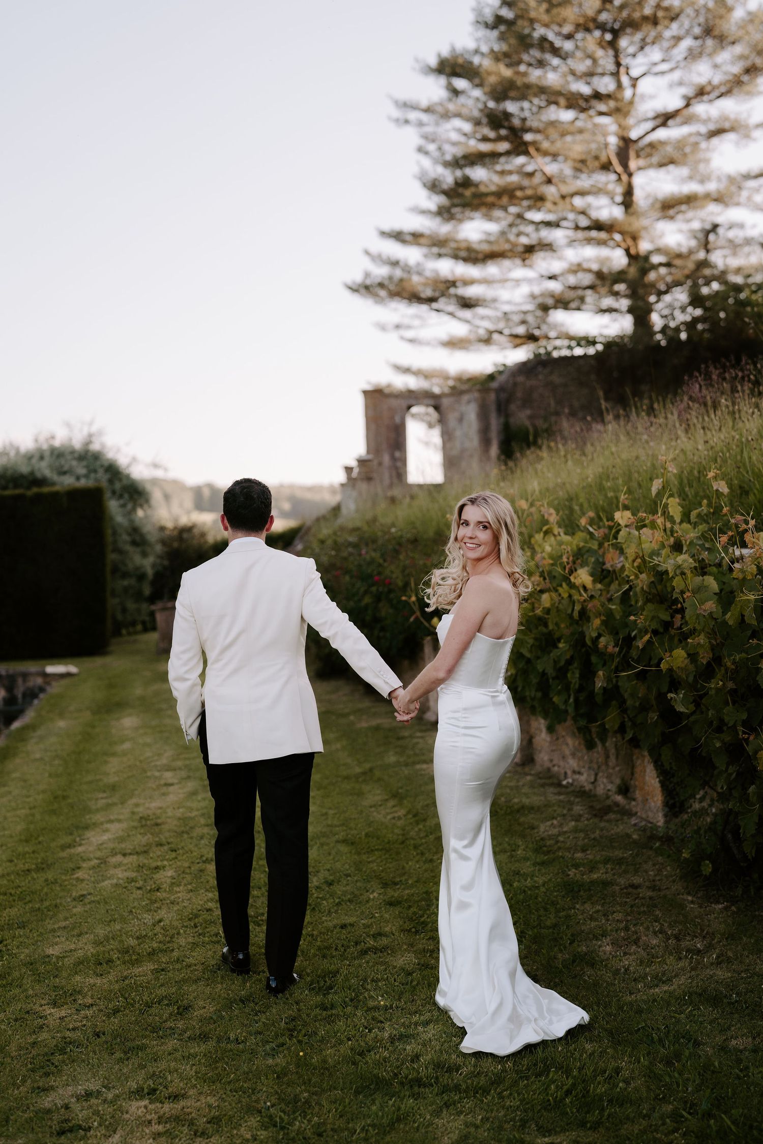 bride smiling over her shoulder while groom leads her away at hamswell house wedding in bath