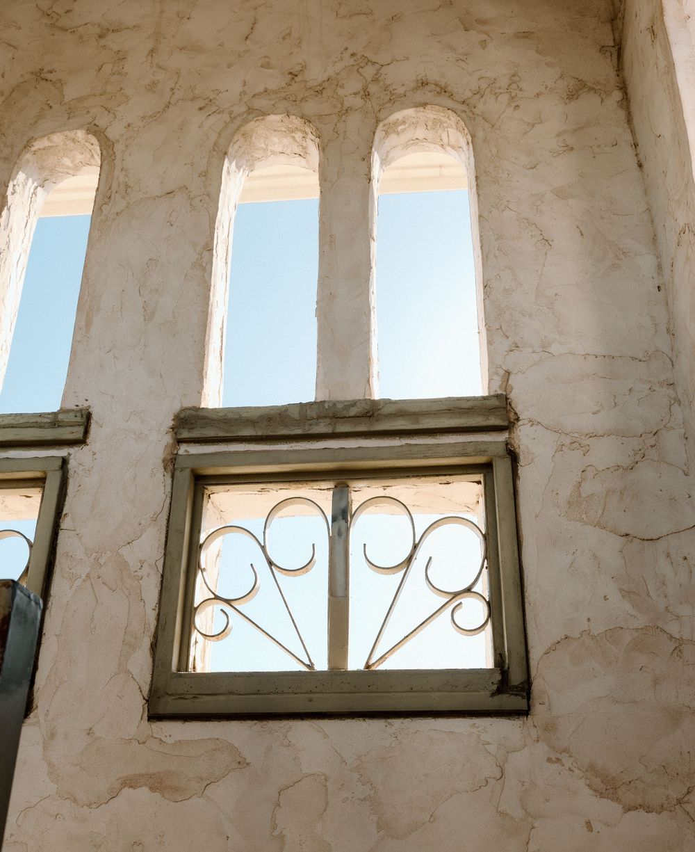 View looking up at white stucco wall with ornate arched windows and decorative ironwork details in Spanish colonial style.