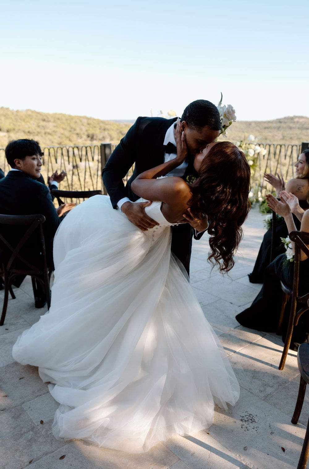 A romantic dip kiss between newlyweds in formal wedding attire against a scenic desert backdrop during their ceremony.